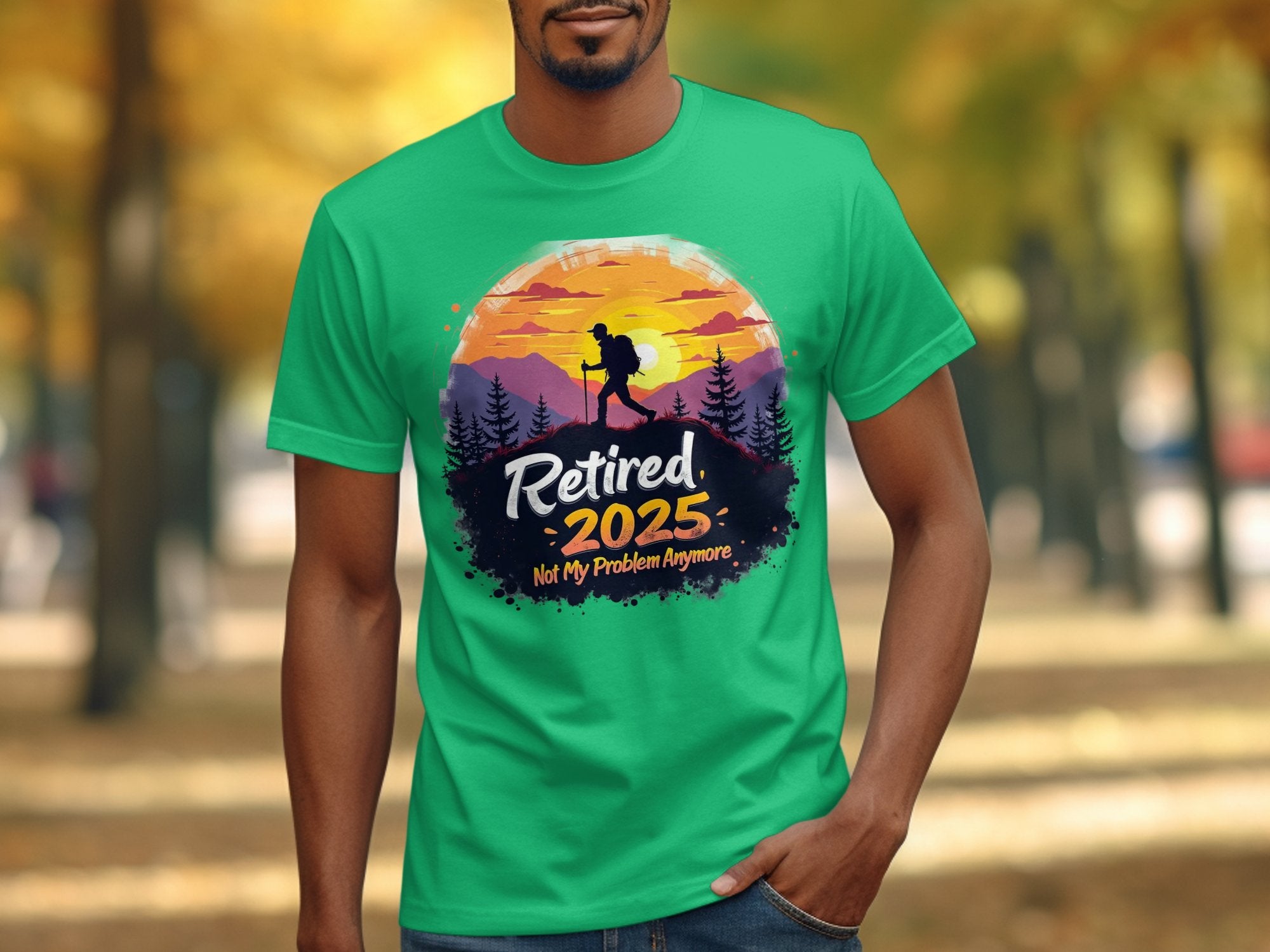 In a park, a person wears Garment Graphics green Retired 2025 T-shirt, showcasing a hiker silhouette, trees, and a sunset with Not My Problem Anymore text. The background displays blurred trees.