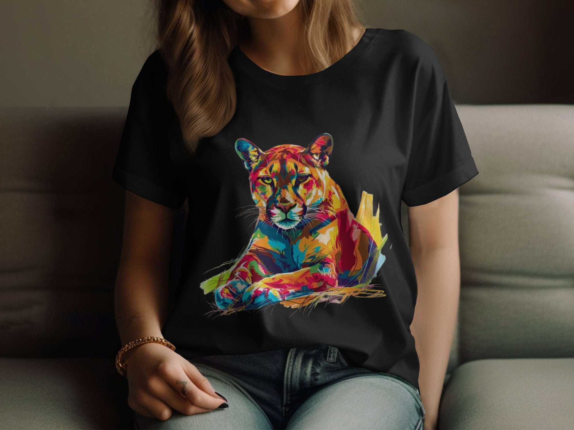 A person relaxes on a couch wearing a black Garment Graphics T-shirt featuring a vivid puma design in vibrant red, blue, yellow, and orange hues on a dark background.