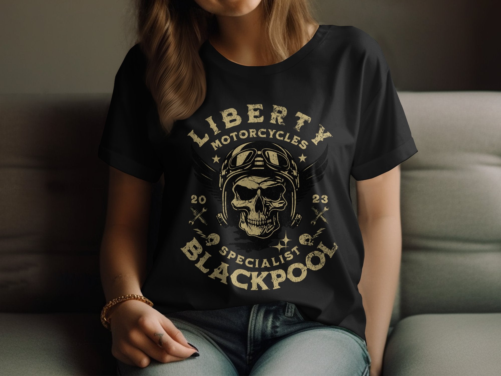 A person in a Garment Graphics Blackpool T-shirt, showcasing a skull with goggles and helmet, relaxes on the couch. The shirts text reads Liberty Motorcycles Specialist Blackpool 2023.