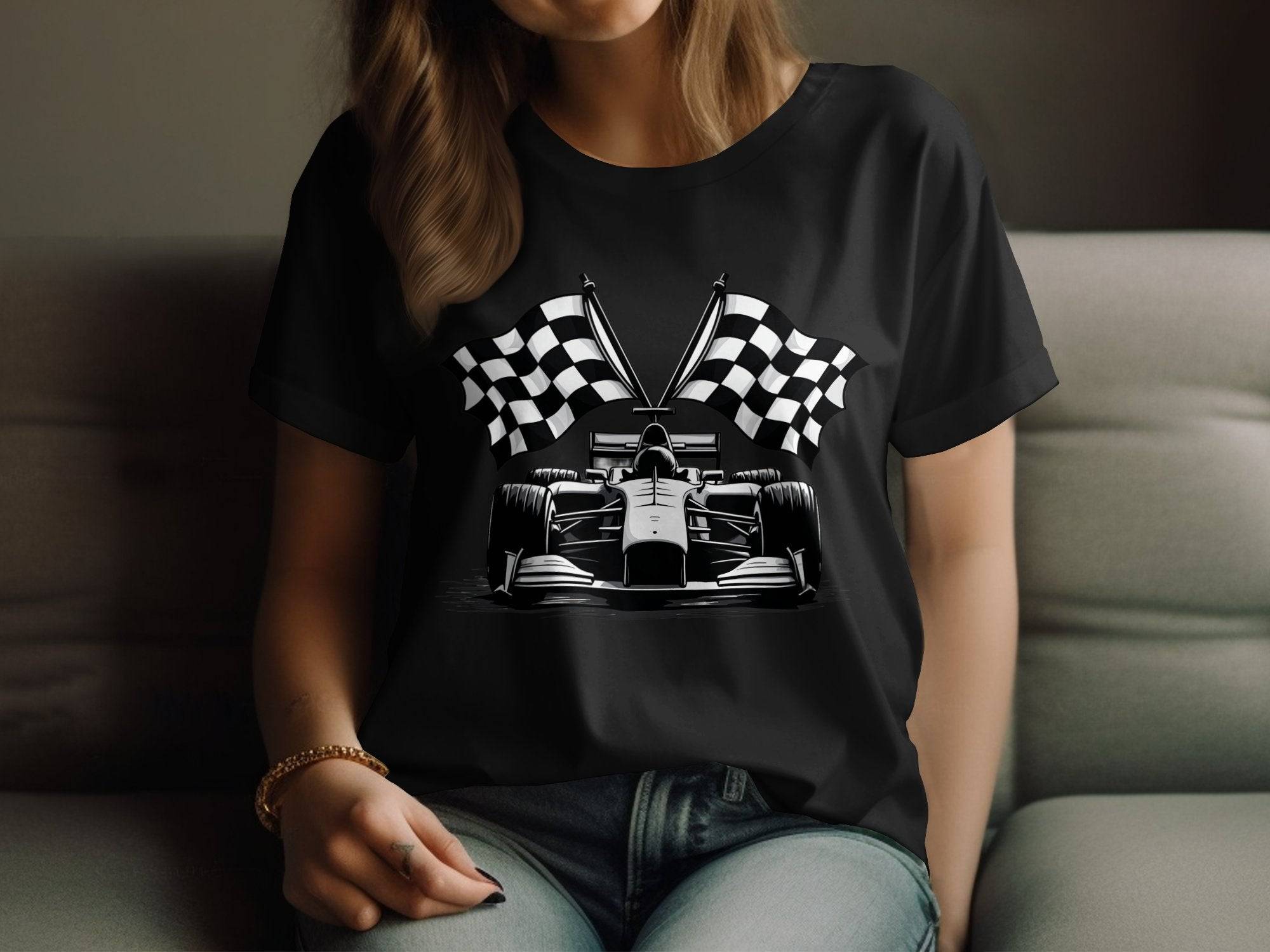 A motorsport enthusiast with long hair sits on a couch, wearing a black Garment Graphics t-shirt featuring a race car and crossed checkered flags, complemented by a stylish bracelet on their wrist.