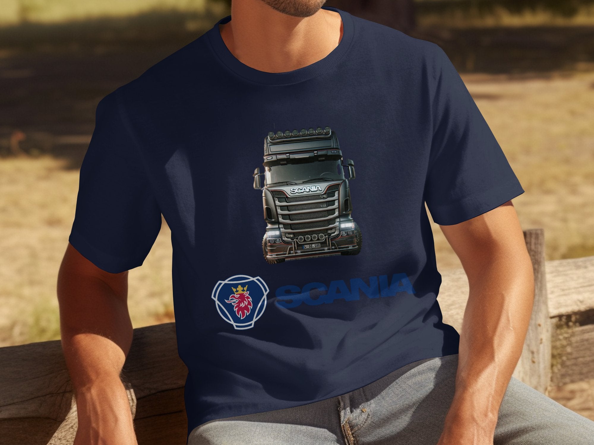A person sits on a bench, proudly wearing a Garment Graphics navy blue T-shirt featuring an illustration of a Scania truck and the iconic Scania logo, perfect for true truck enthusiasts.