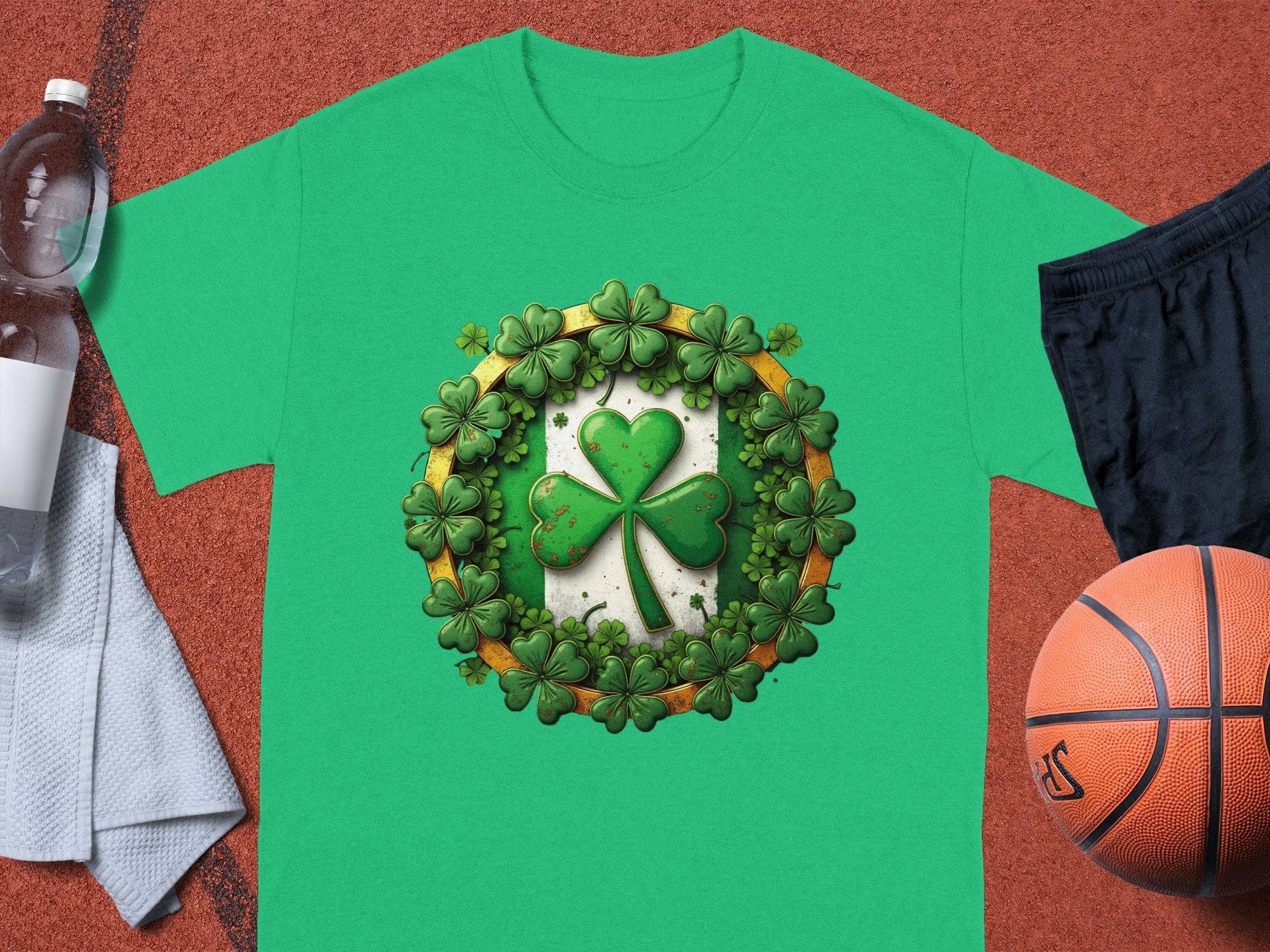 A green graphic T-shirt by Garment Graphics, featuring a shamrock wreath design, is on a basketball court. Nearby are a basketball, black shorts, a clear water bottle, and a white towel—a sporty way to celebrate St. Patricks Day.