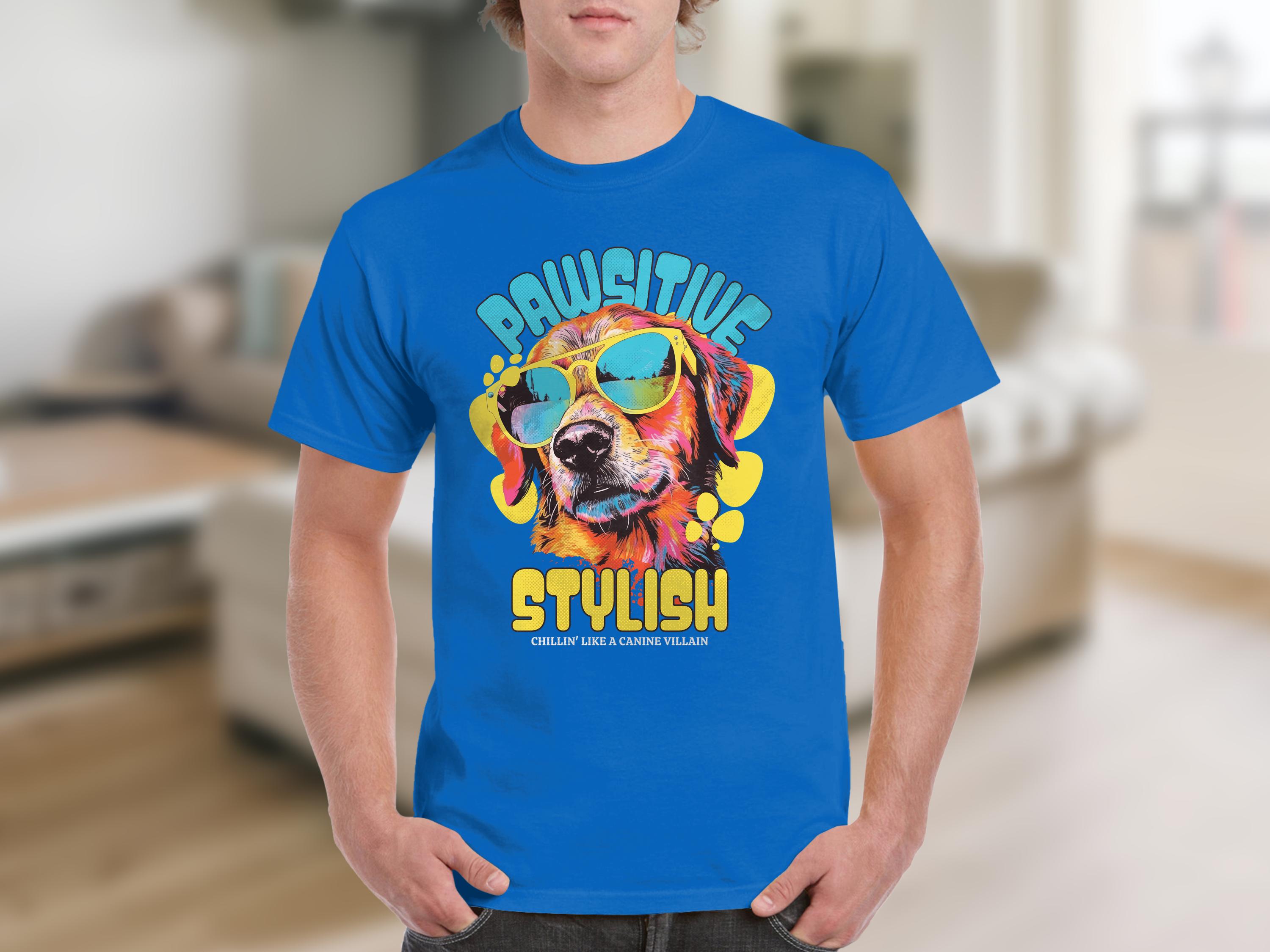 Someone wears a blue Dog T-shirt by Garment Graphics, featuring a vibrant dog graphic with sunglasses. The phrases Paw-sitive Stylish and Chillin Like A Canine Villain in bold, playful fonts make it pop against the softly blurred room interior.