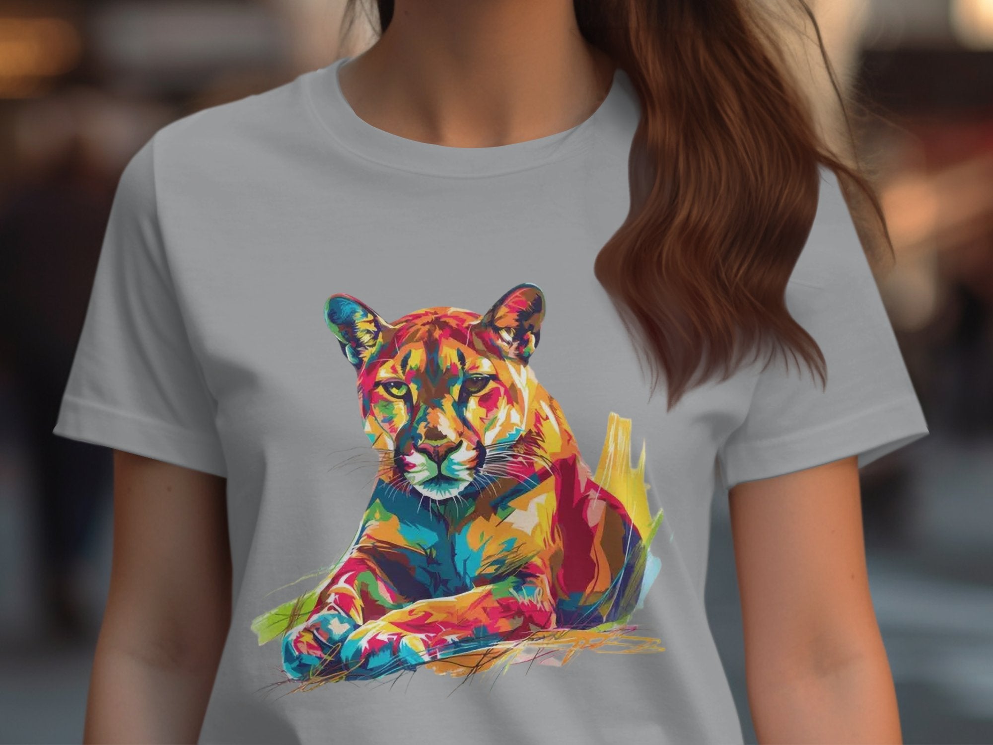 A person wearing a Garment Graphics light grey T-shirt featuring a colorful puma design with vibrant shades of red, orange, blue, and yellow in a stylized illustration of a resting cougar. Their hair is long and brown.