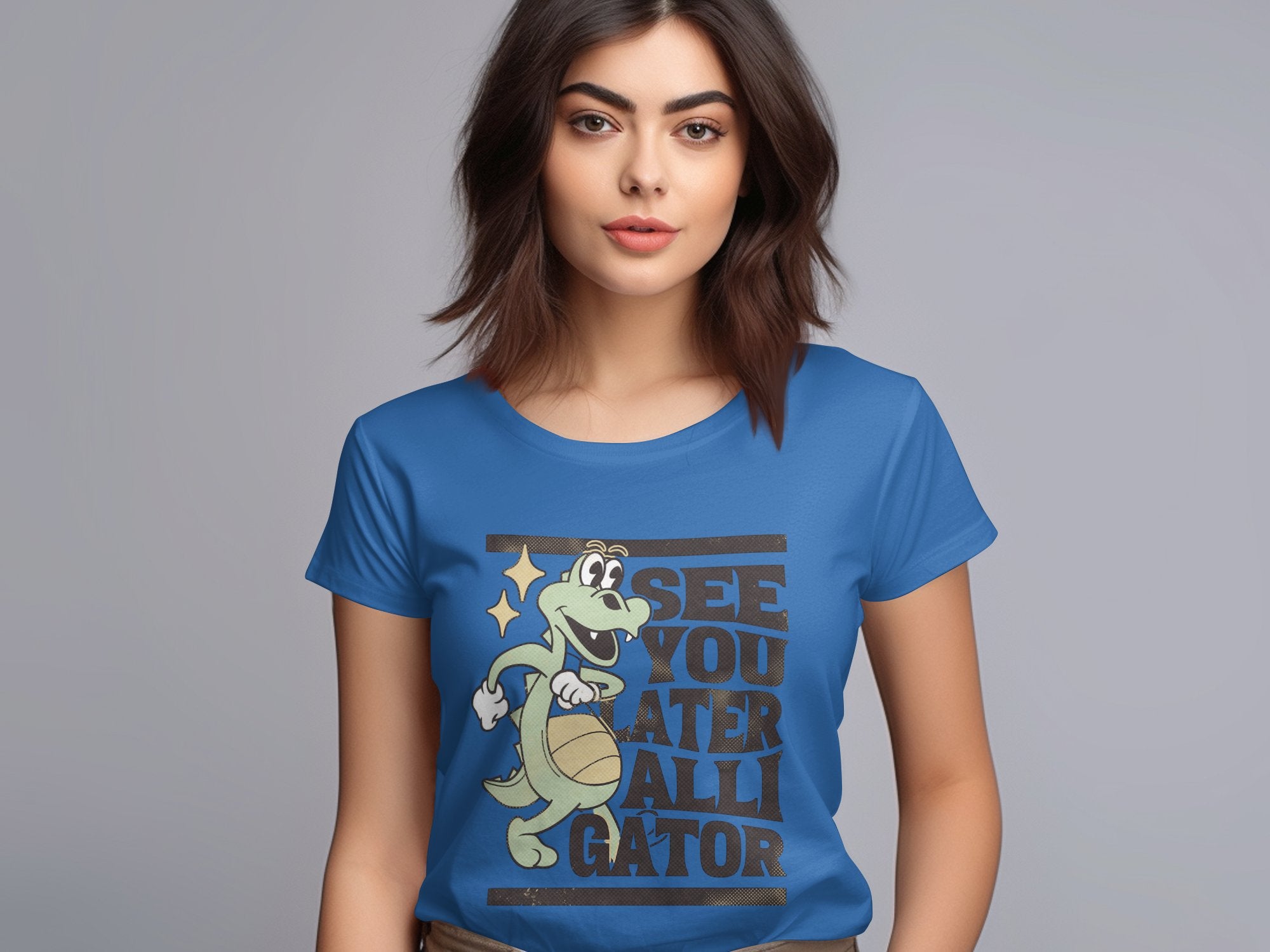 A person in a blue Garment Graphics t-shirt featuring a cartoon alligator holding a basketball and star, with the phrase See you later alligator. With dark hair against a plain backdrop, its an ideal choice for those seeking stylish womens sizing.
