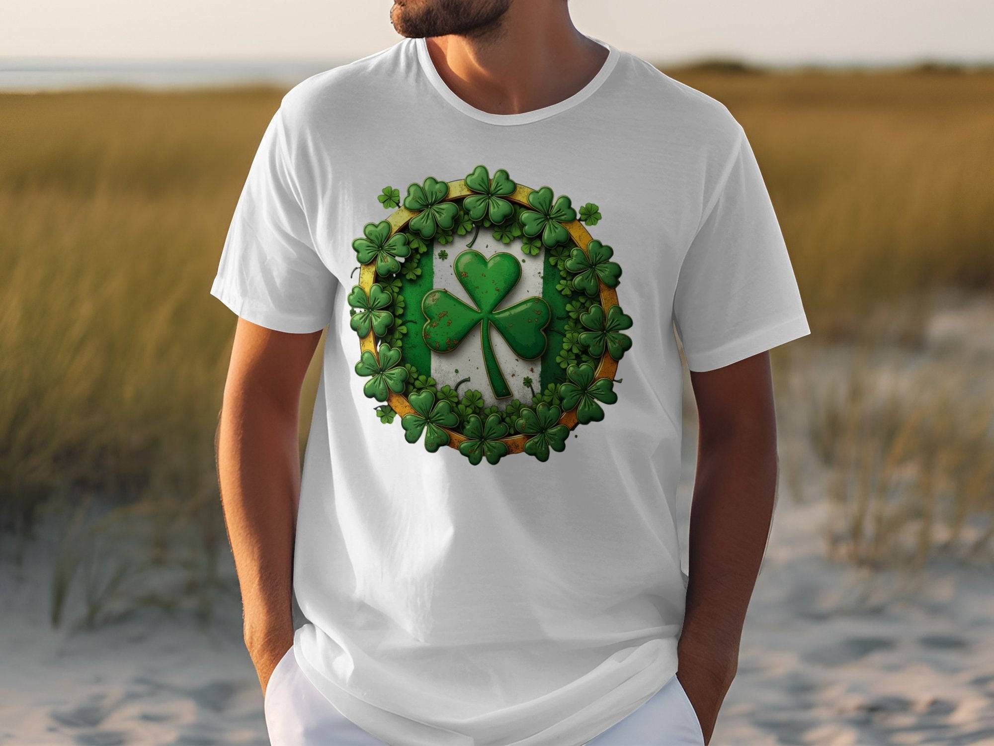A person in a Garment Graphics white T-shirt featuring a green shamrock and circular orange-accented leaf pattern stands in tall grass, capturing the St. Patricks Day spirit.