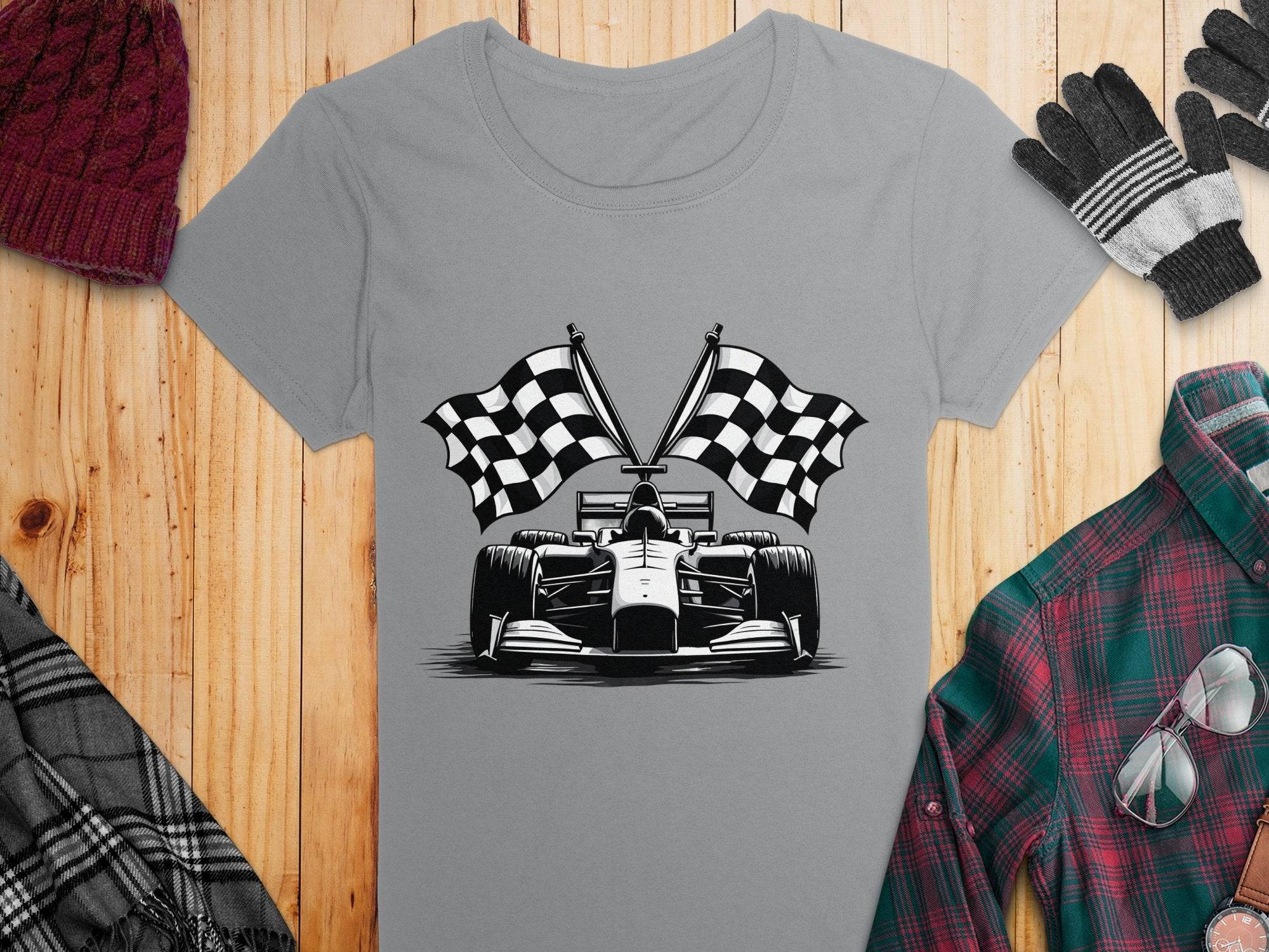 Garment Graphics gray T-shirt showcases a black-and-white race car with crossed checkered flags, ideal for motorsport fans. Its paired with a red plaid shirt, scarf, gloves, and maroon knit beanie on a wooden surface.