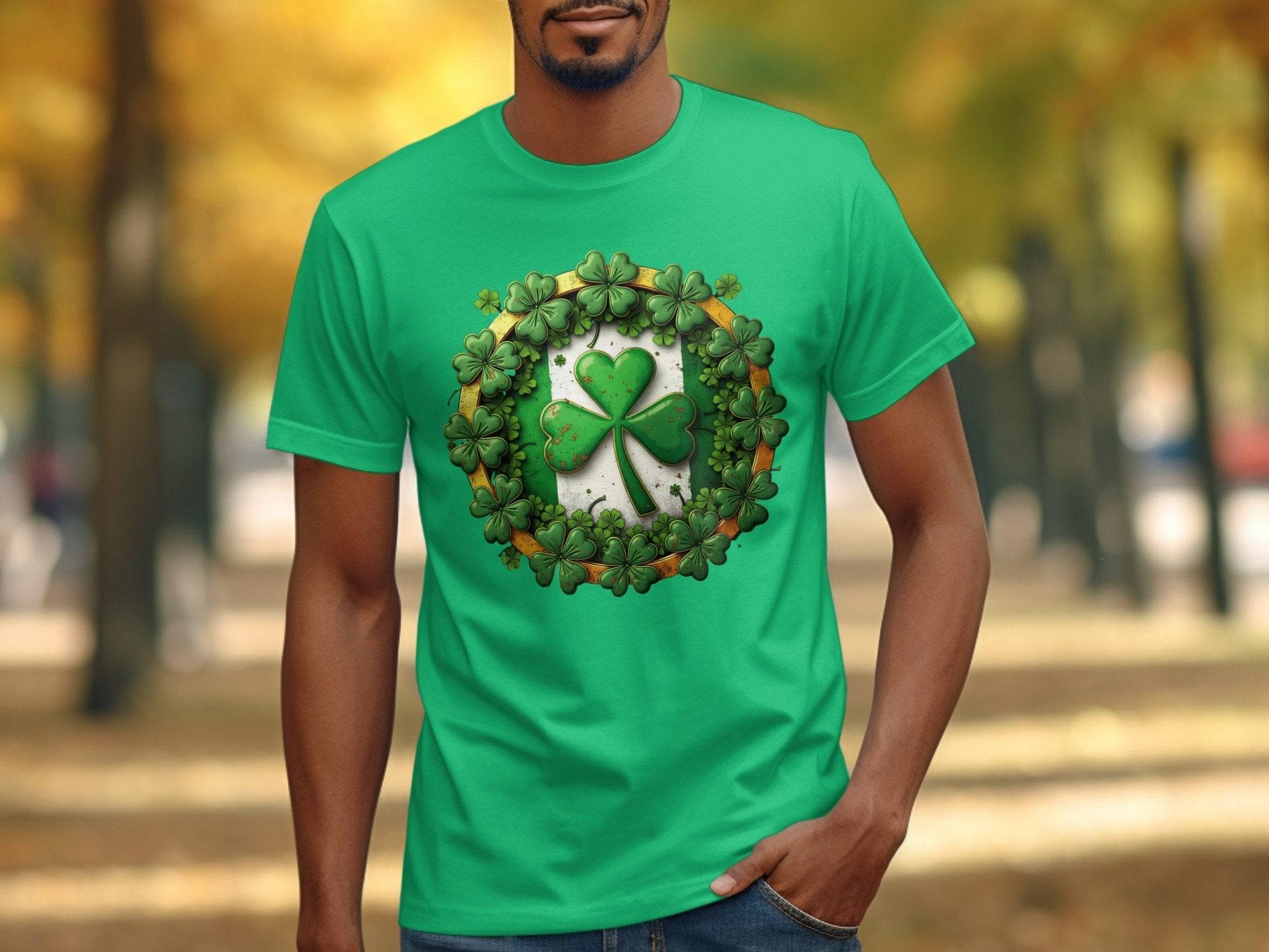 A person wears a Garment Graphics green T-shirt with a large St. Patricks Day shamrock surrounded by smaller shamrocks, while standing outside against blurred autumn foliage, casually placing one hand in their pocket.