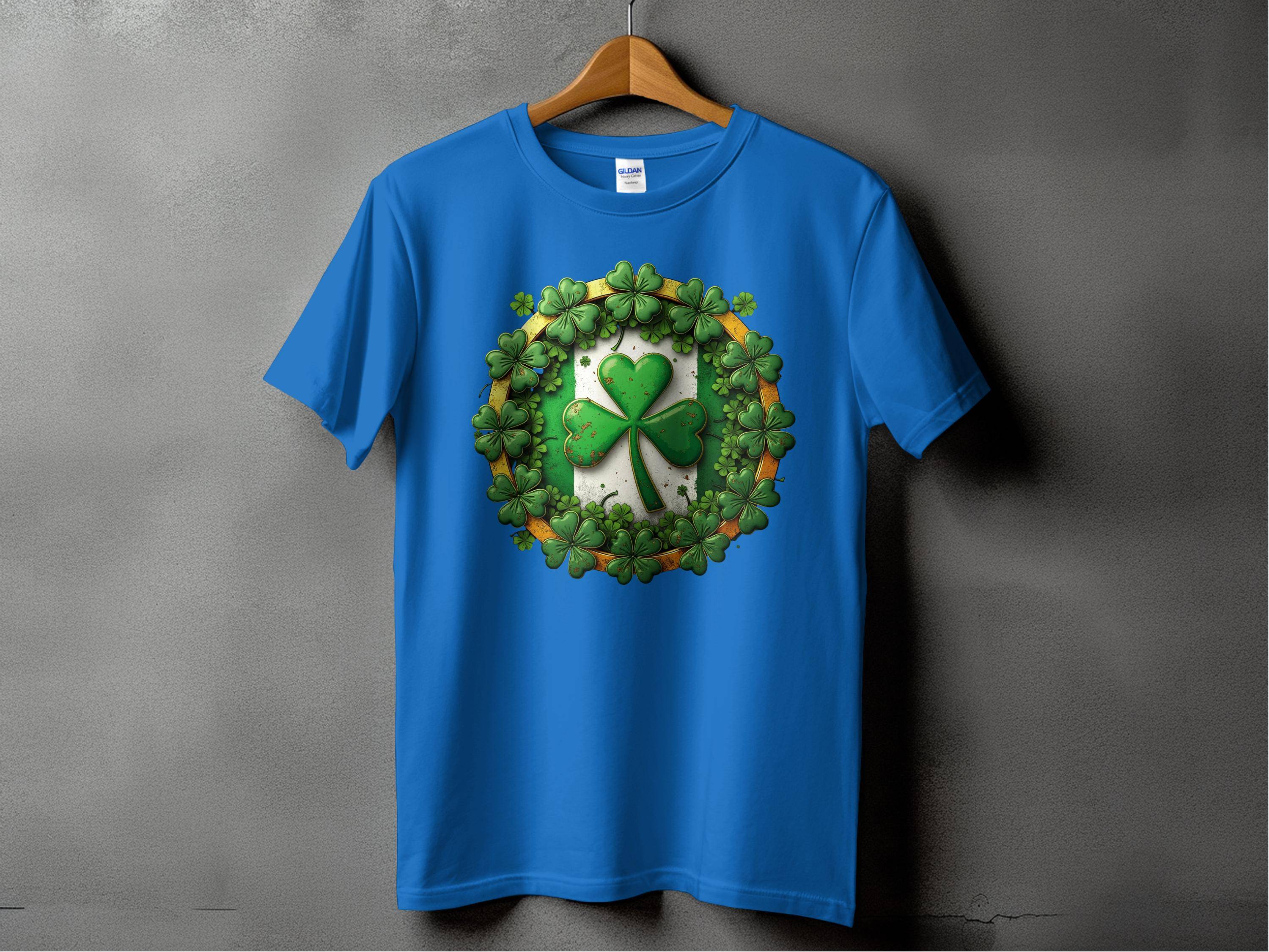 A Garment Graphics blue graphic T-shirt with a circular design featuring a large green shamrock surrounded by smaller ones hangs on a wooden hanger against a gray backdrop, ideal for St. Patricks Day celebrations.