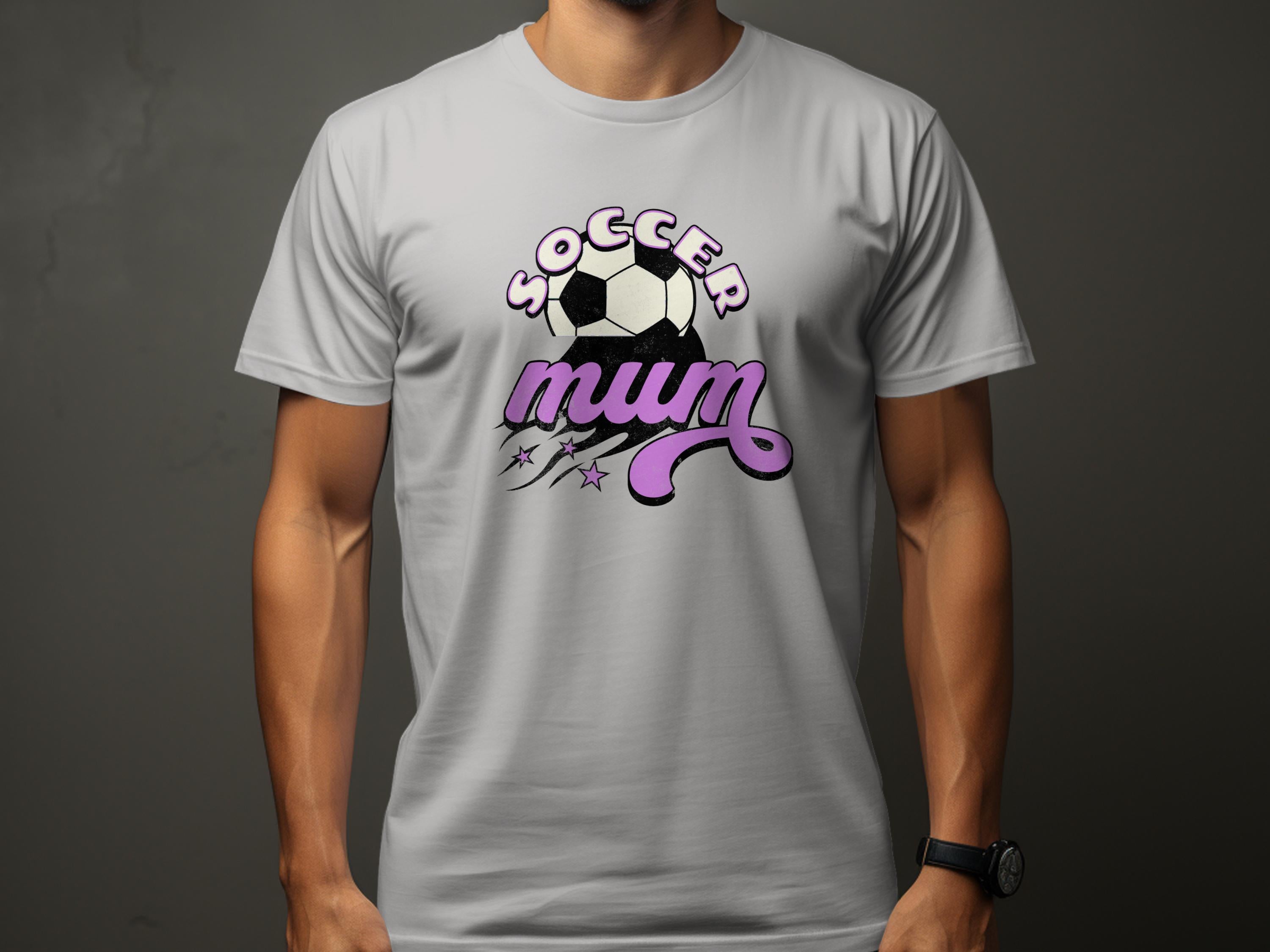 A person is wearing Garment Graphics classic fit light gray T-shirt with Soccer Mum in pink cursive, featuring a soccer ball and small stars on a plain dark background.