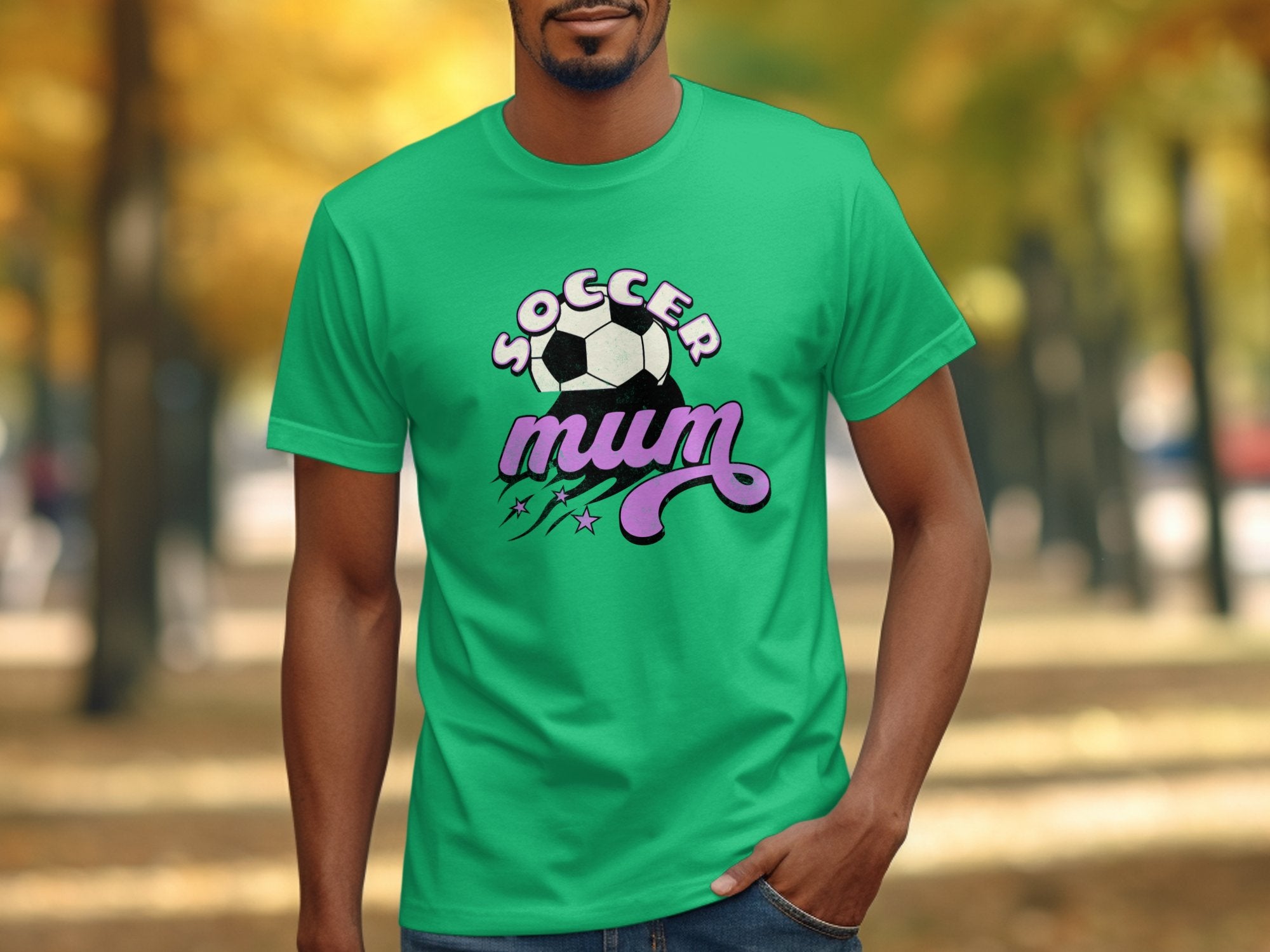 In an outdoor park, a man wears a Garment Graphics classic fit green T-shirt featuring the bold Soccer Mum slogan and a soccer ball graphic. The blurred walkway and trees enhance this vibrant, stylish design.