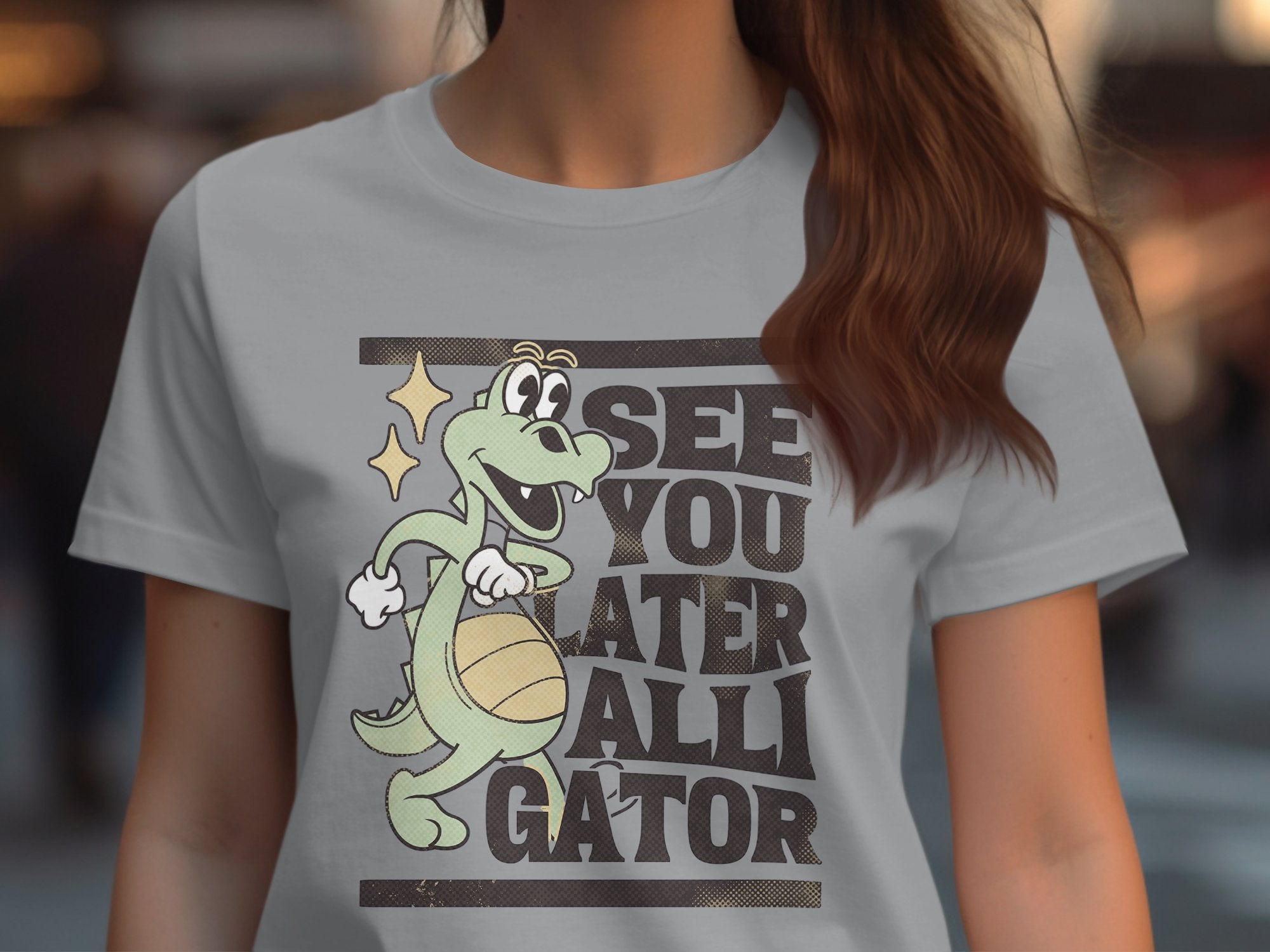 Wearing a Garment Graphics Alligator T-Shirt in light gray, this tee features a cartoon alligator holding a basketball with the bold text SEE YOU LATER ALLIGATOR, available in womens sizes.