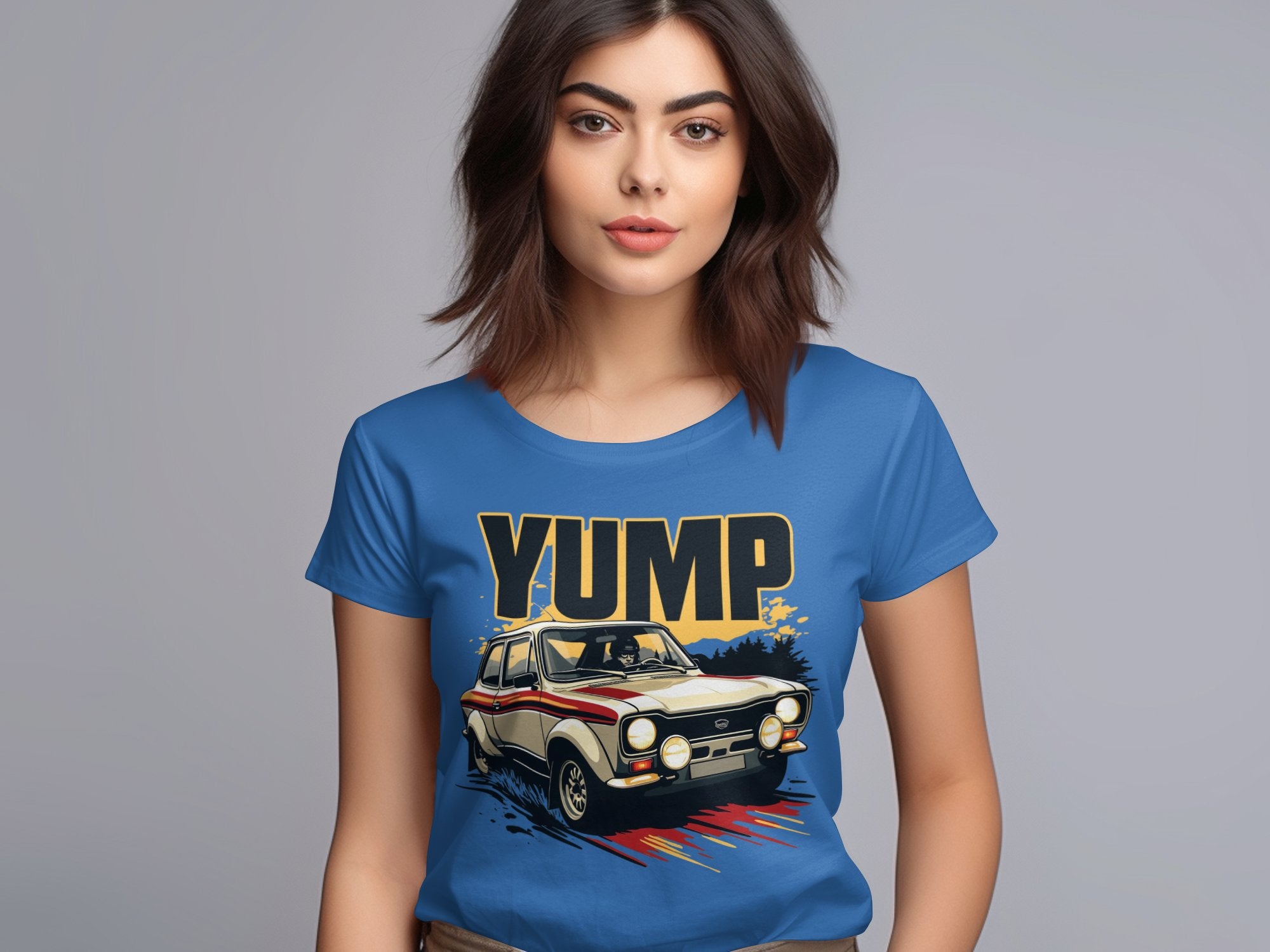A dark-haired woman wears a blue t-shirt featuring a bold vintage racing car graphic and YUMP lettering by Garment Graphics, set against a plain gray background.