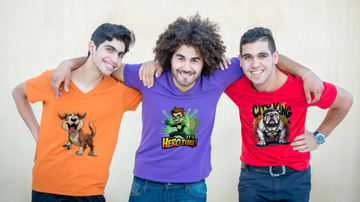 Three friends smiling, standing with arms around each other, wearing graphic t-shirts: one orange with a cartoon dog, one purple with Its Hero Time!, and one red with City King and a bulldog. They are against a beige background.