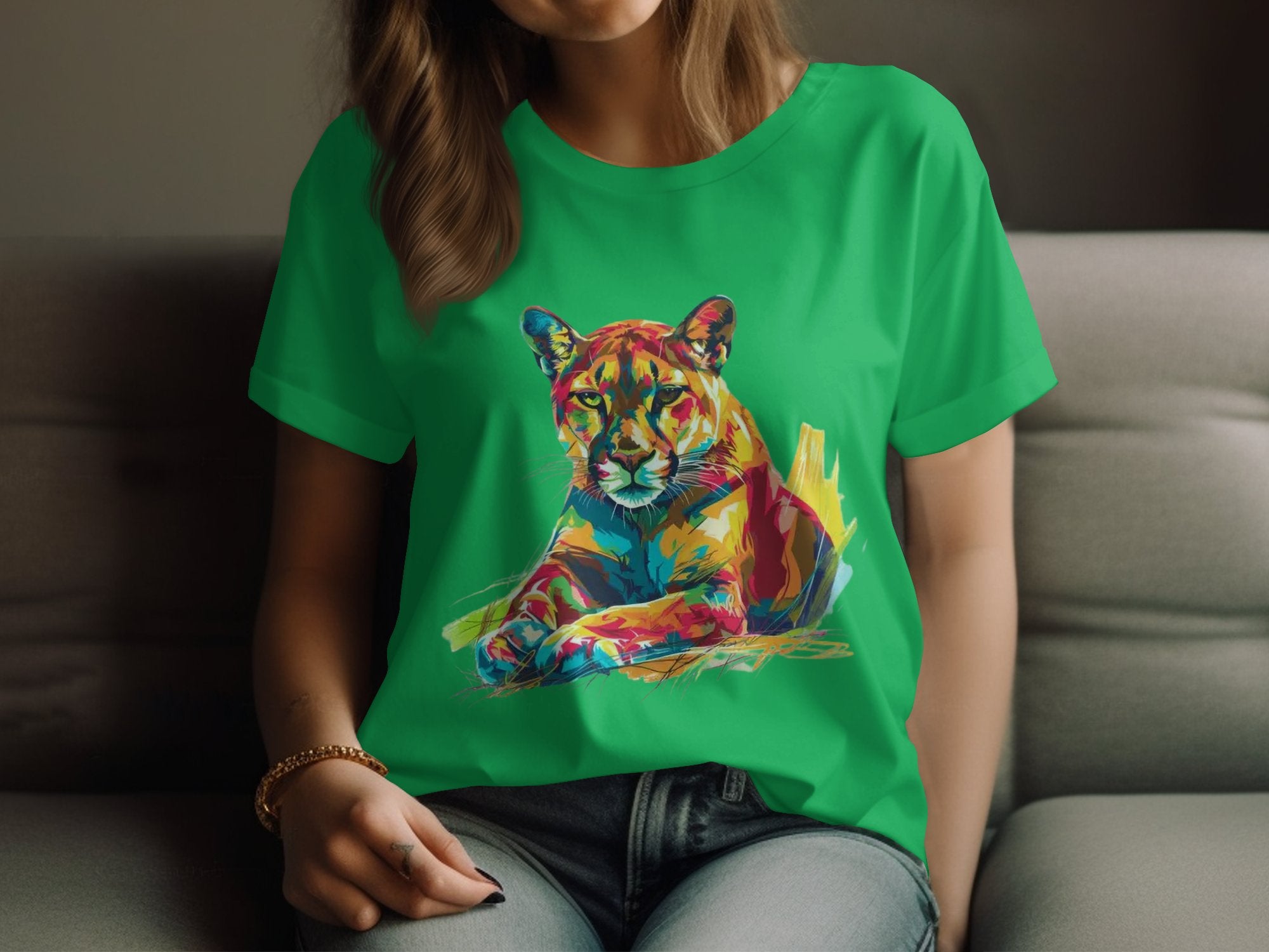A person sits on a couch in a Garment Graphics green T-shirt featuring an abstract colorful panther design. The vibrant print is eye-catching, though their face isnt visible.
