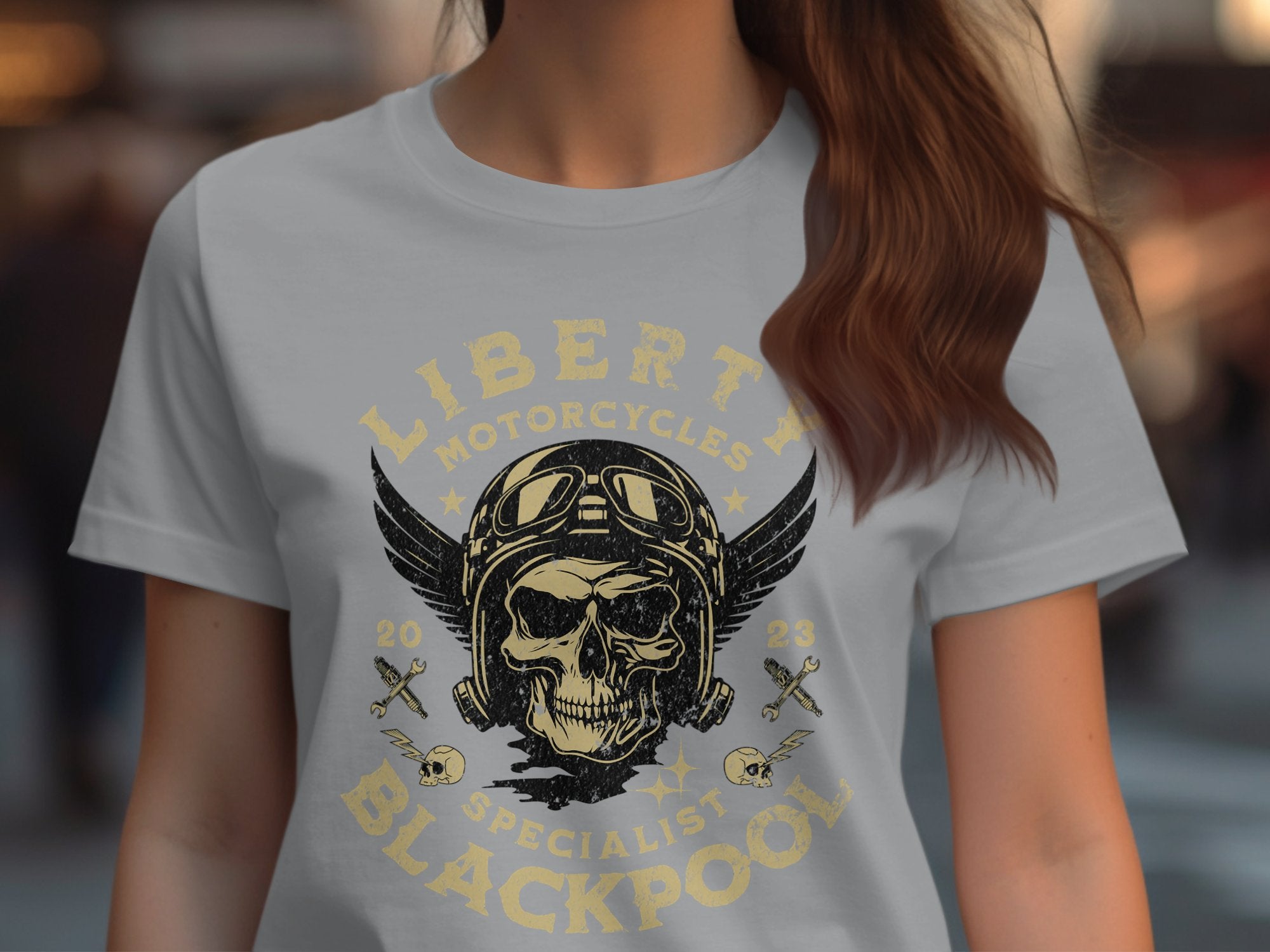 A person wears a Garment Graphics Blackpool-themed T-shirt with a skull in goggles and helmet, wings, and Liberty Motorcycles Specialist Blackpool 2023 above crossed pistons, embodying motorcycling spirit.