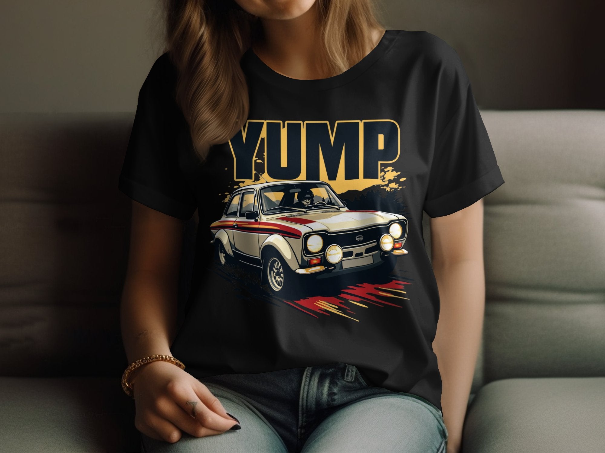 Dressed in jeans, a person relaxes on a couch wearing a black Garment Graphics T-shirt featuring a bold vintage racing car design with YUMP above it, embodying the retro T-shirt vibe. Their long hair cascades over one shoulder, enhancing the casual look.