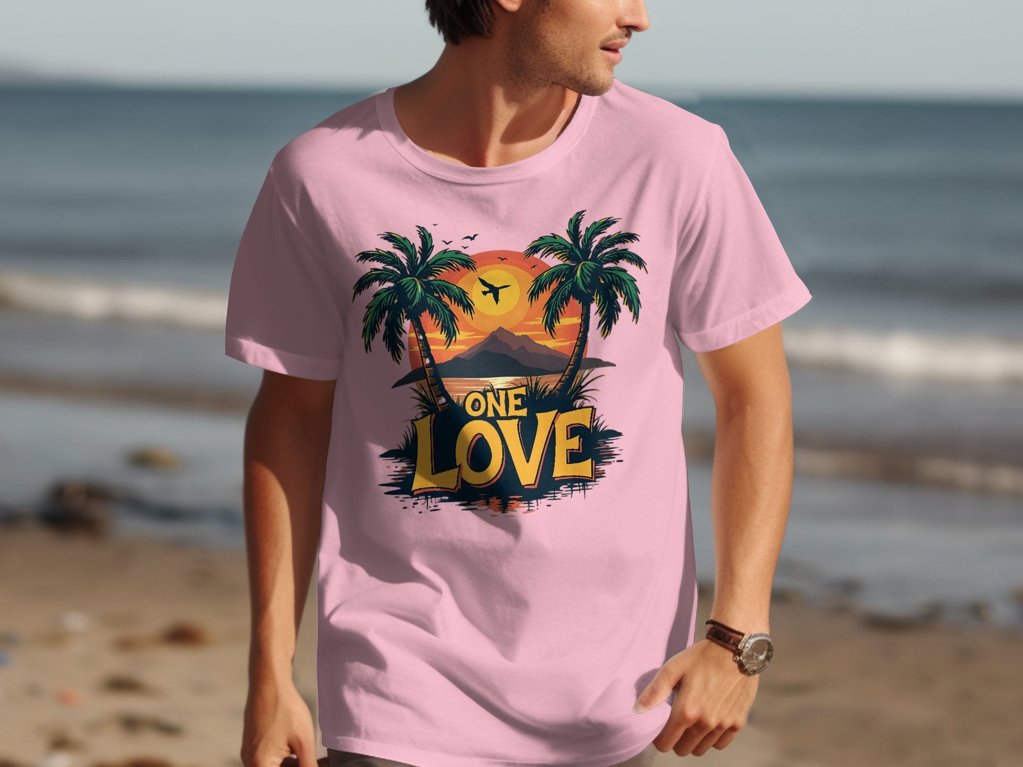 A beachgoer dons a Garment Graphics pink t-shirt featuring palm trees, a tropical sunset, and ONE LOVE text. The tranquil ocean stretches behind them, creating an idyllic scene for beach enthusiasts.