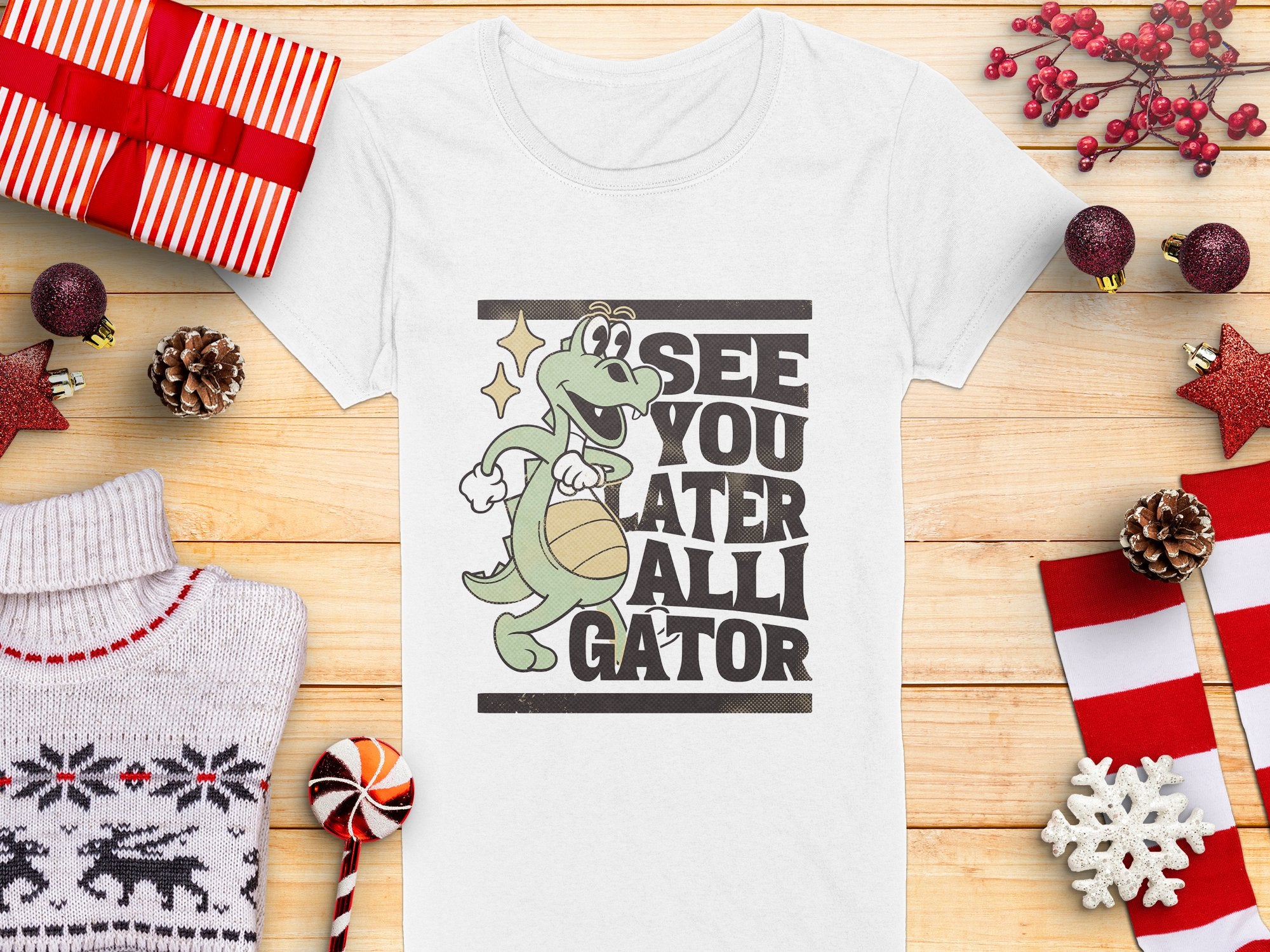 Garment Graphics offers a humorous womens white T-shirt featuring a cartoon alligator holding a basketball with See You Later Alligator text, set against holiday-themed elements like red-and-white gifts, pinecones, and knitted sweater decorations.