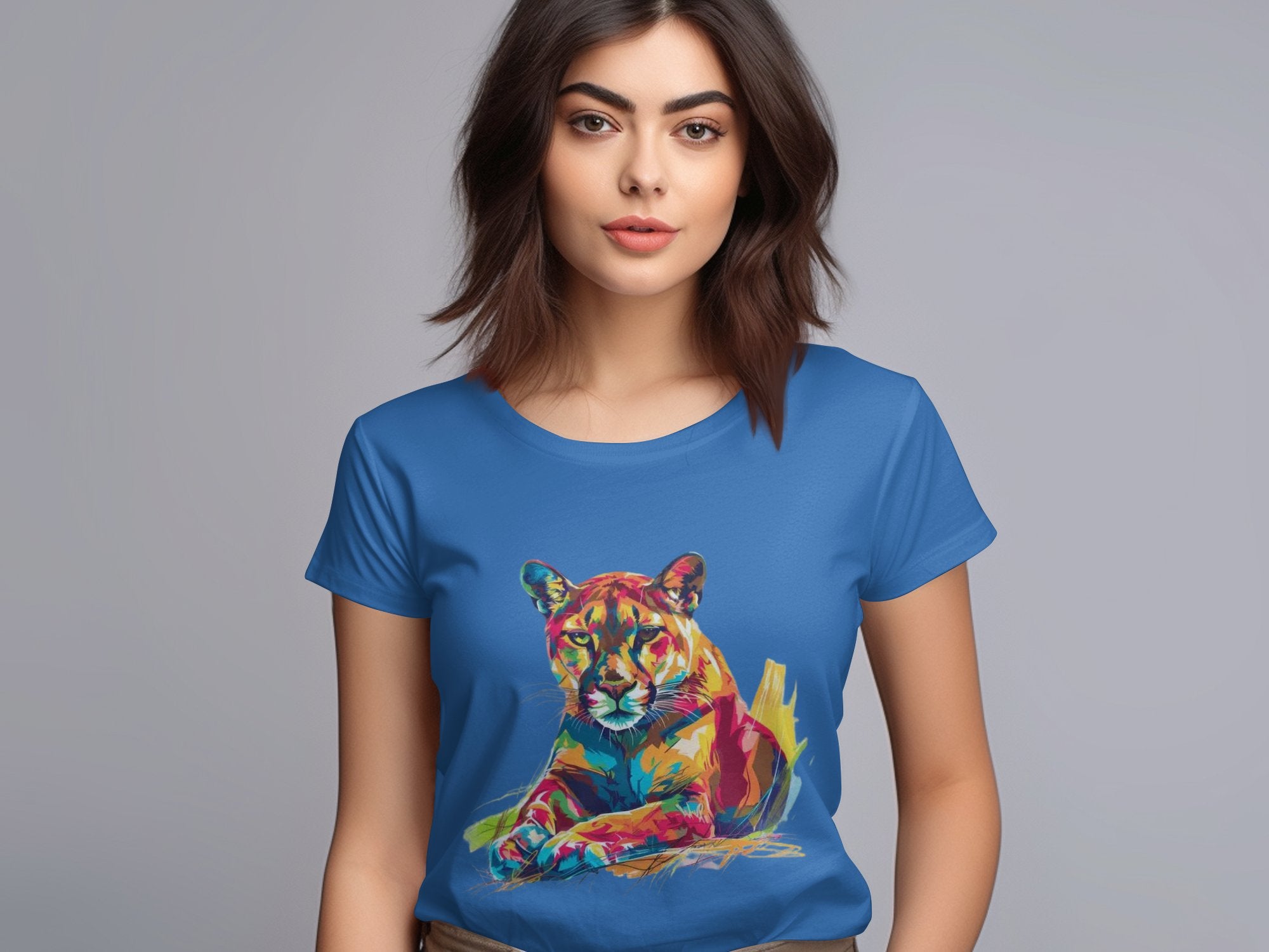 A woman with shoulder-length brown hair wears a Garment Graphics blue T-shirt featuring a colorful puma design. The vibrant graphic stands out against the plain gray background, highlighting its striking illustration.