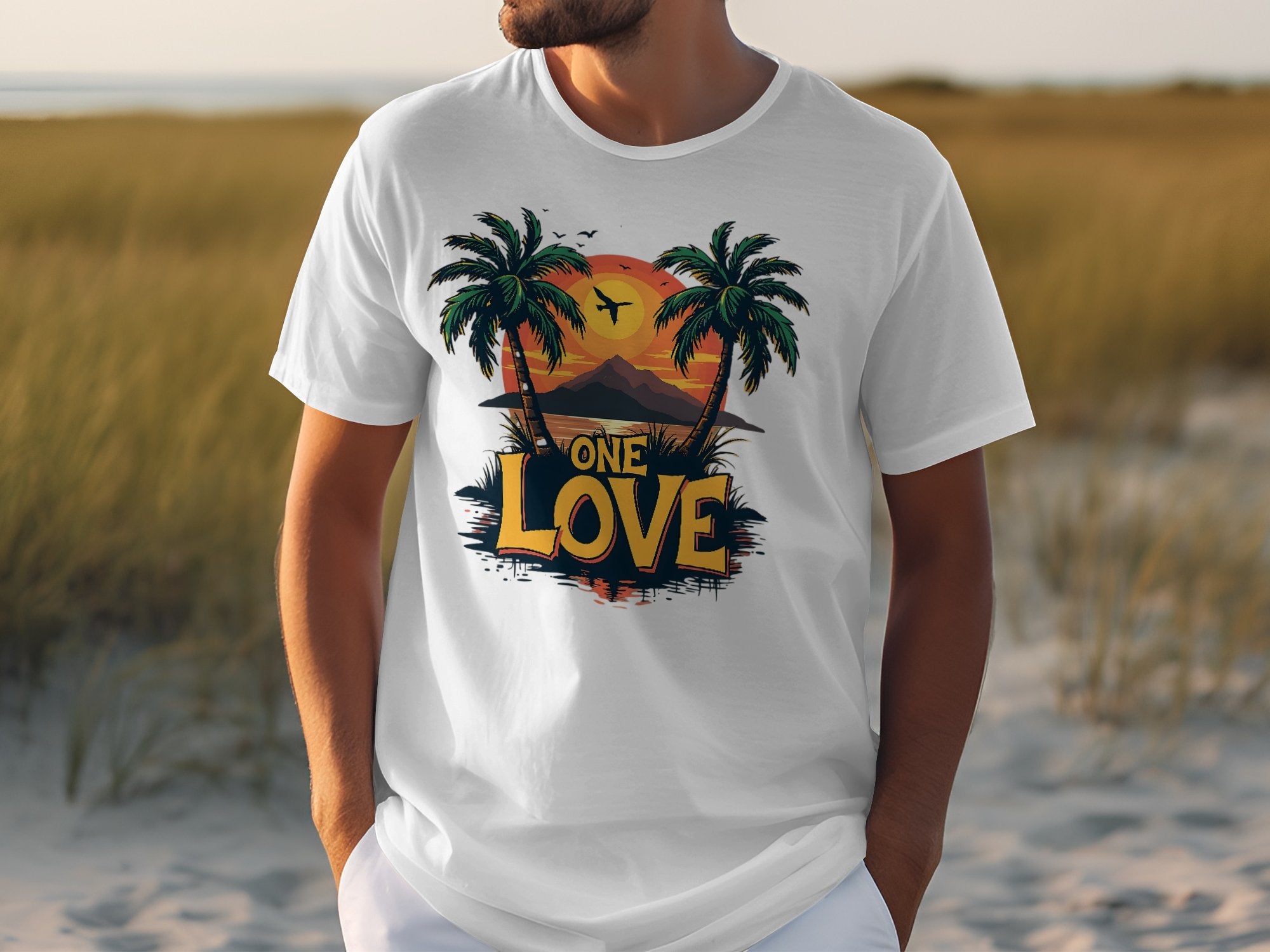 A person in a Garment Graphics white cotton T-shirt featuring two palm trees, a tropical sunset, a mountain, and a plane with One Love in bold yellow and black letters stands outdoors on grass, perfect for beach lovers dreaming of distant shores.