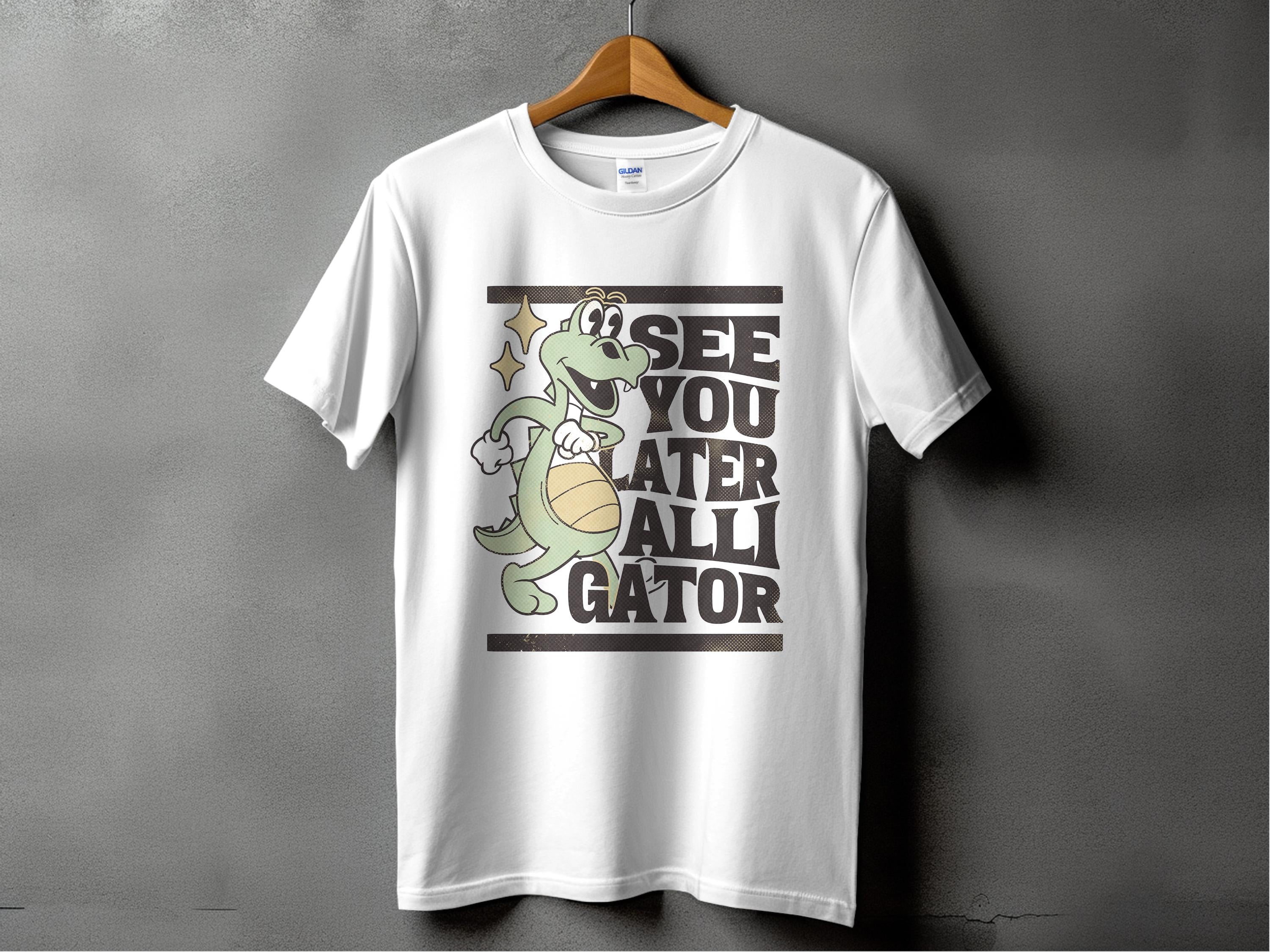 Against a gray background, a white tee by Garment Graphics hangs on a wooden hanger. Ideal for casual outings, it displays a cartoon alligator with a basketball and the phrase SEE YOU LATER ALLIGATOR, encapsulating playful style effortlessly.