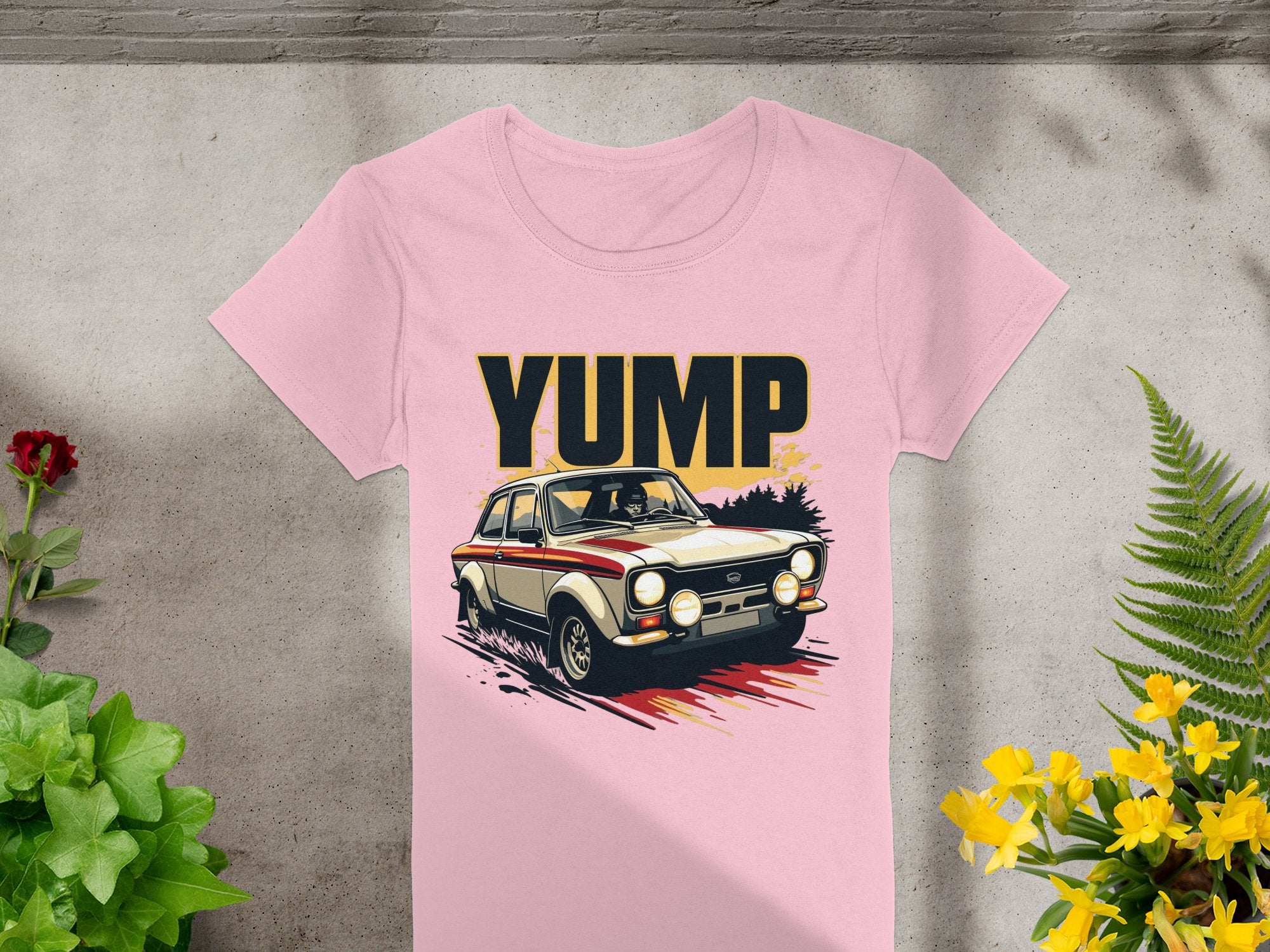 Garment Graphics pink retro T-shirt showcases a vintage racing car with YUMP boldly printed. The design is set against green and yellow plants on a light concrete background, emphasizing its bold graphic appeal.