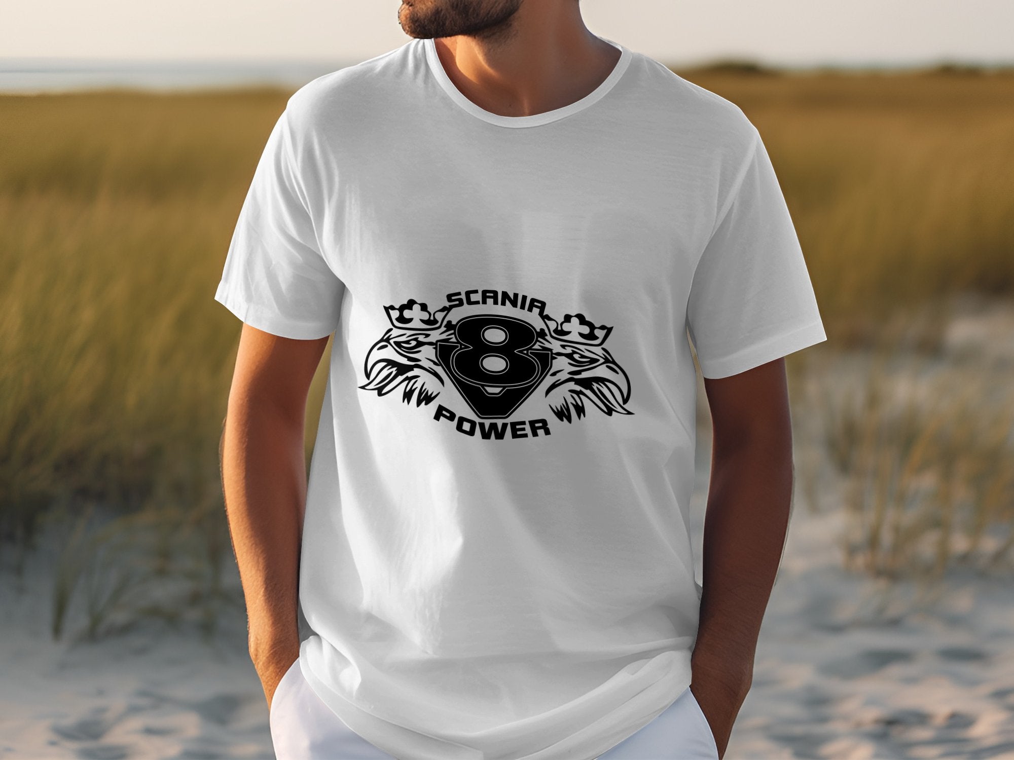 An individual outdoors on sandy dunes, wearing a Garment Graphics white tee with a Scanir Power logo, featuring a stylized number 8 and two lion-like designs.