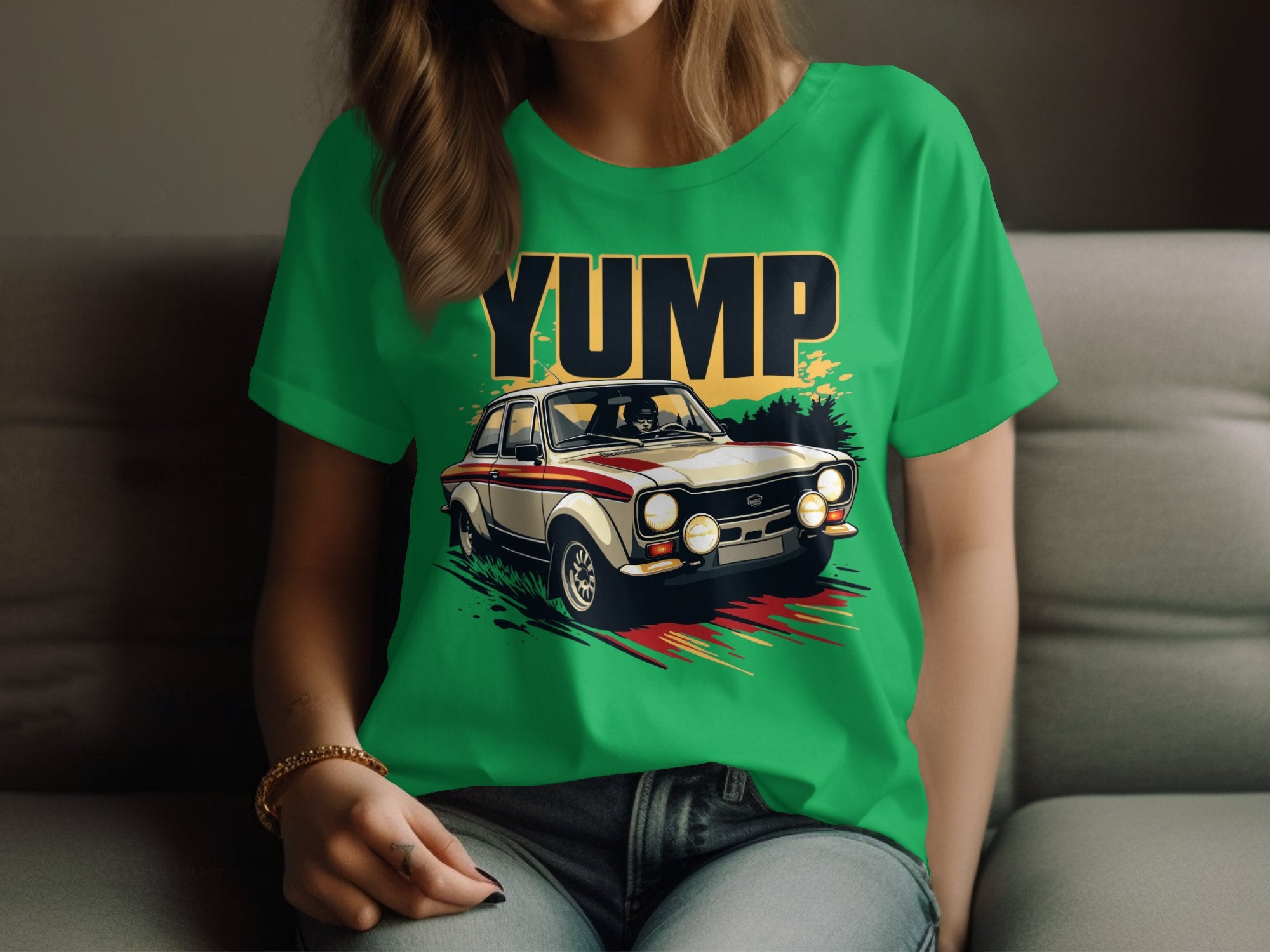 A person lounges on a couch in a green Garment Graphics T-shirt featuring a vintage racing car with the word YUMP in bold letters, stripe details, and large headlights. Theyre paired with jeans and a bracelet.