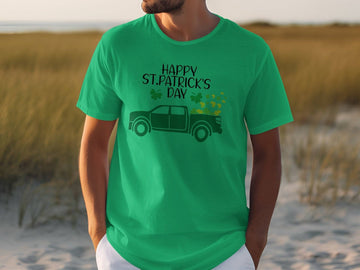 A man in a Garment Graphics green T-shirt with Happy St. Patricks Day proudly showcases Irish pride alongside a truck adorned with shamrocks, set against a sandy backdrop with grass, creating a festive atmosphere.