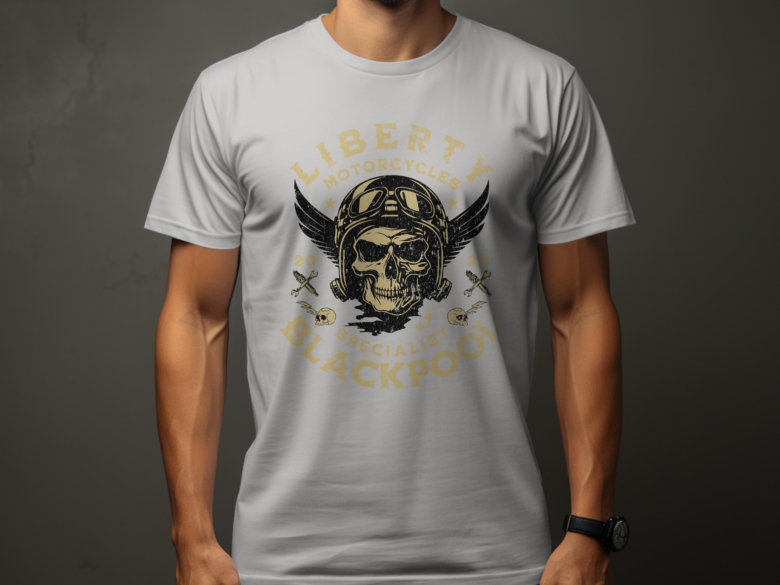 A person wears a vintage gray t-shirt by Garment Graphics featuring a winged skull in a helmet. The words LIBERTY MOTORCYCLES appear above and SPECIALISTS BLACKPOOL below, with crossed wrenches on each side, ideal for motorcycle enthusiasts.