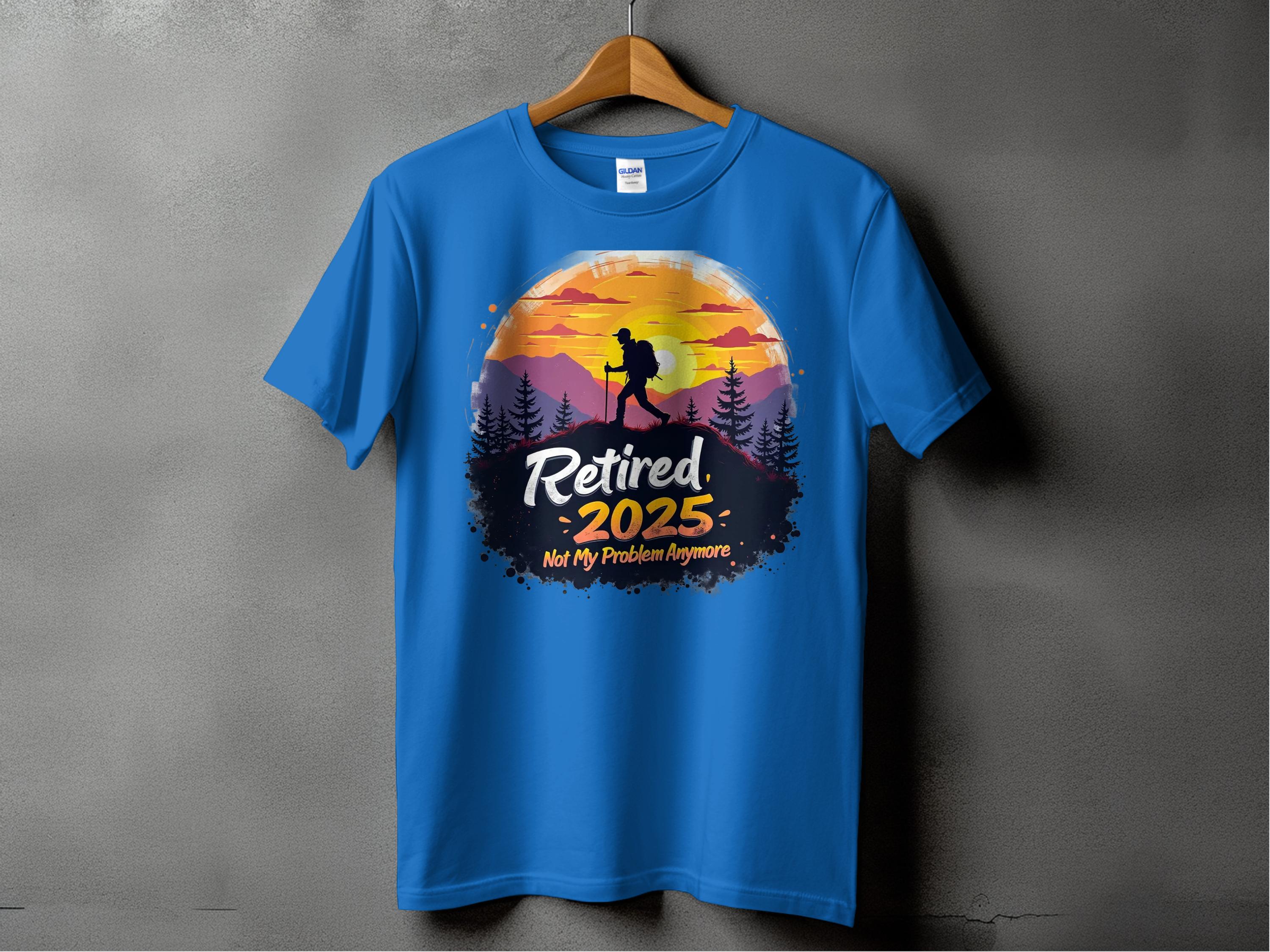 A blue sunset T-shirt by Garment Graphics hangs on a wooden hanger against a gray backdrop. It showcases a hiker with a sunset and mountains, featuring the text Retired 2025. Not My Problem Anymore.