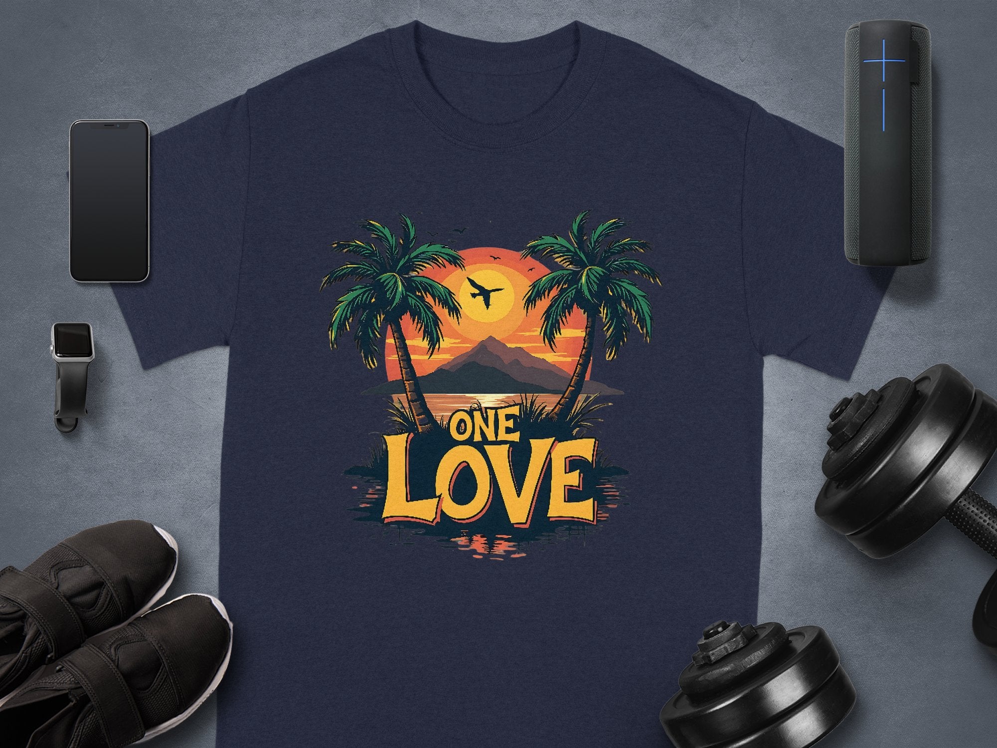 A Garment Graphics navy blue T-shirt features a tropical sunset, palm trees, mountain silhouettes, and One Love. Alongside, theres a smartphone, smartwatch, wireless speaker, shoes, and adjustable dumbbells. Ideal for beach enthusiasts.
