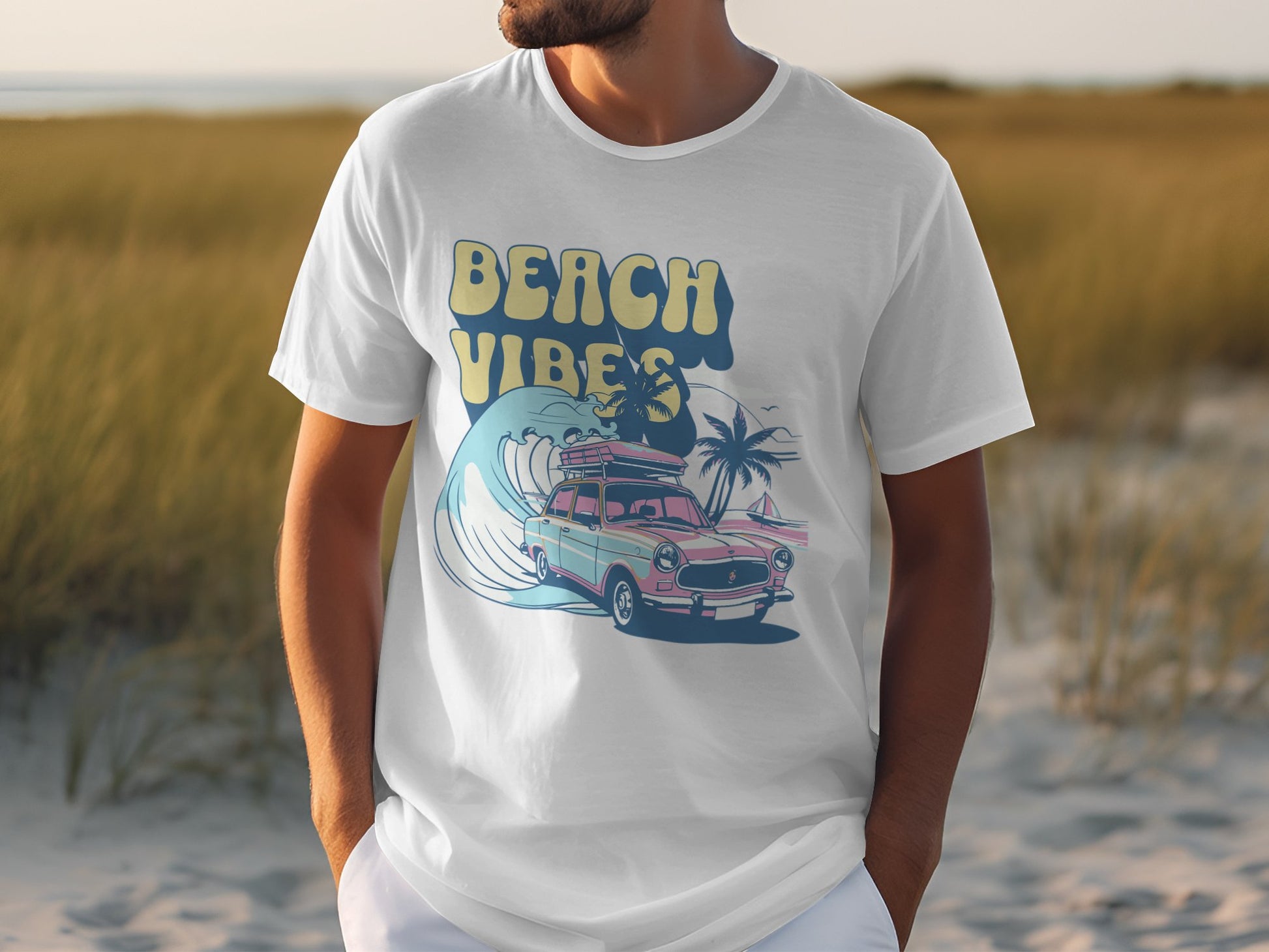 A person wears a white Garment Graphics t-shirt featuring a classic car with surfboards, palm trees, and waves. The vibrant design highlights the words Beach Vibes. Sand and grass provide an ideal backdrop for this summery scene.