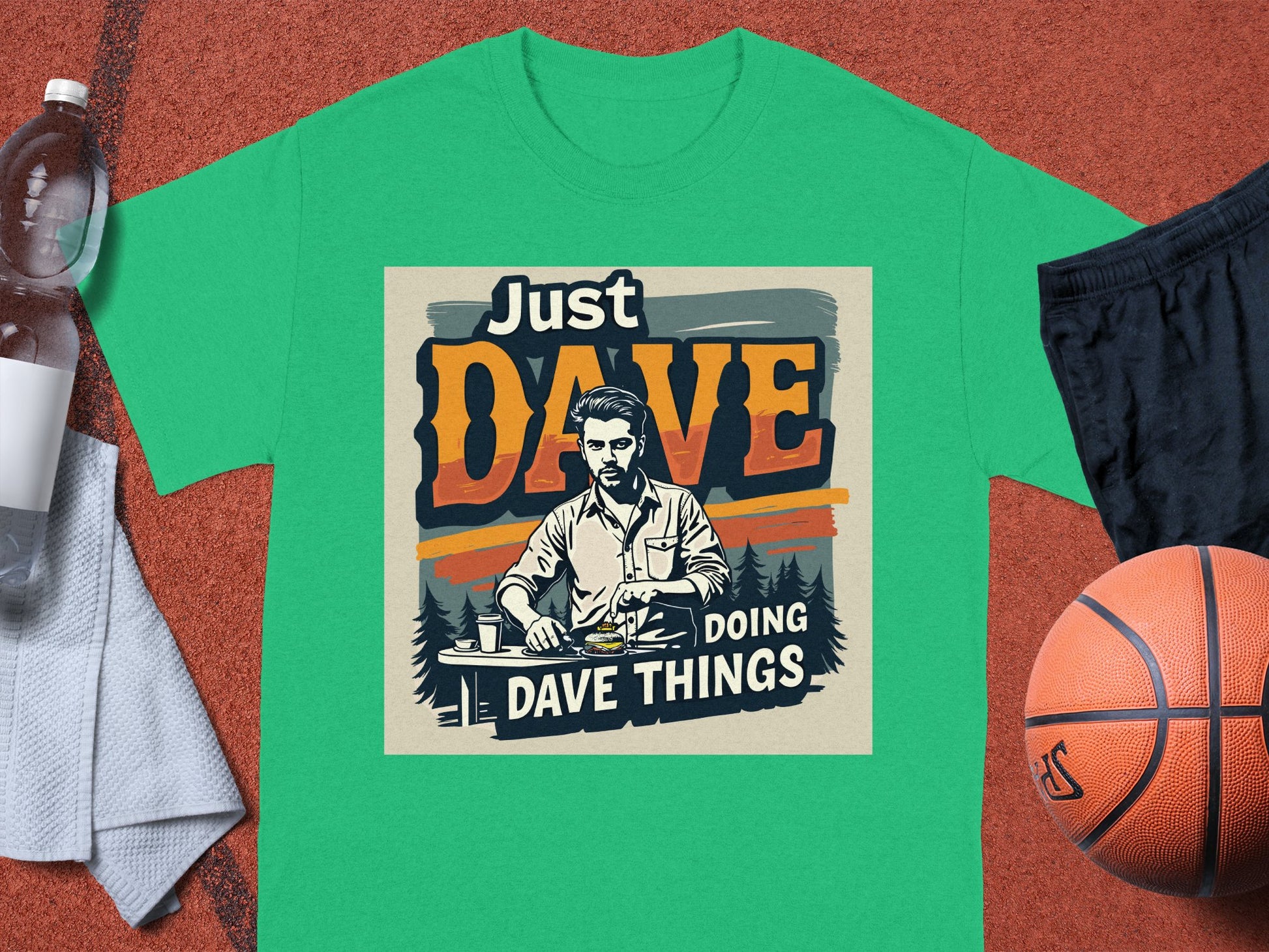 A classic fit graphic tee by Garment Graphics: green with a mustached man dining at a table. Features bold Just Dave Doing Dave Things text. Displayed on a basketball court with accessories like a basketball, water bottle, and shorts nearby.