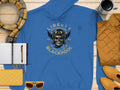 The Garment Graphics blue hoodie displays a Liberty Motorcycle Specialist Blackpool design with a skull, helmet, and wings. Styled on wood with a notebook, pen, yellow scarf, mug, quilted jacket, sunglasses, clutch, and shoes—ideal for those seeking unique fashion from Blackpool.