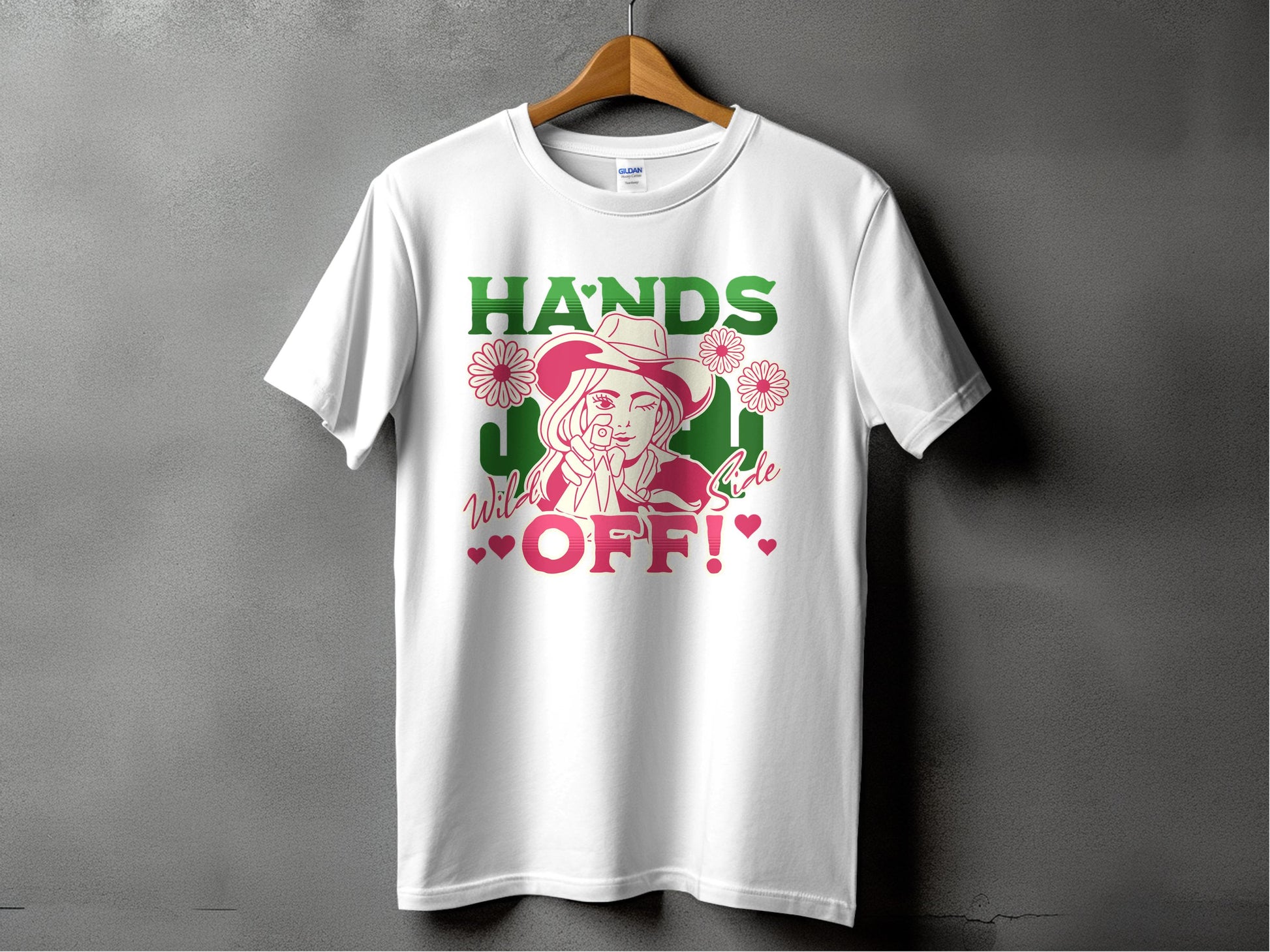 Garment Graphics t-shirt, white on a hanger, showcases a striking design of a hatted figure with two flowers. HANDS OFF! appears in green and red text along with Wild and J. Red hearts are integrated into the classic fit Hands Off T-Shirts design.