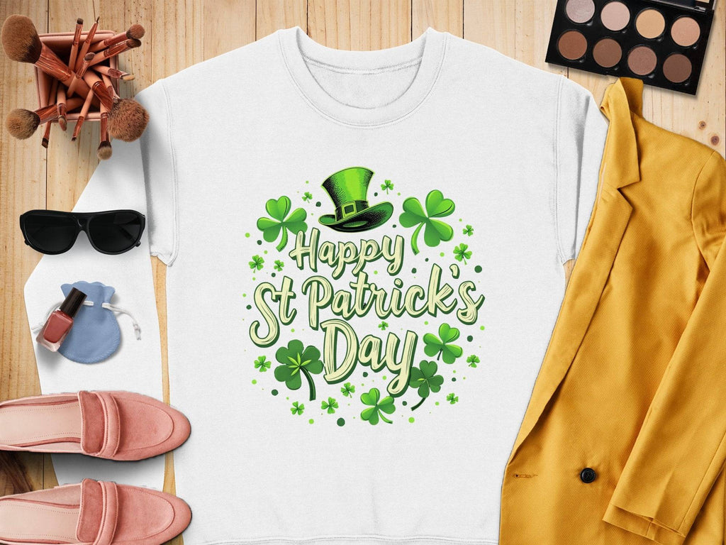 A Garment Graphics white shamrock graphic sweatshirt with Happy St Patricks Day in green text and festive cheer elements, including a green top hat, rests on a wooden surface beside a yellow jacket, pink shoes, sunglasses, a blue pouch, makeup brushes, and a palette.