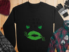 A black Garment Graphics sweatshirt showcases Happy St. Patricks Day in script with green lips and shamrocks, capturing the festive clover kiss vibe. Its stylishly matched on a wooden surface with a red knit hat, black and gray gloves, a plaid green shirt, and a gray plaid scarf.