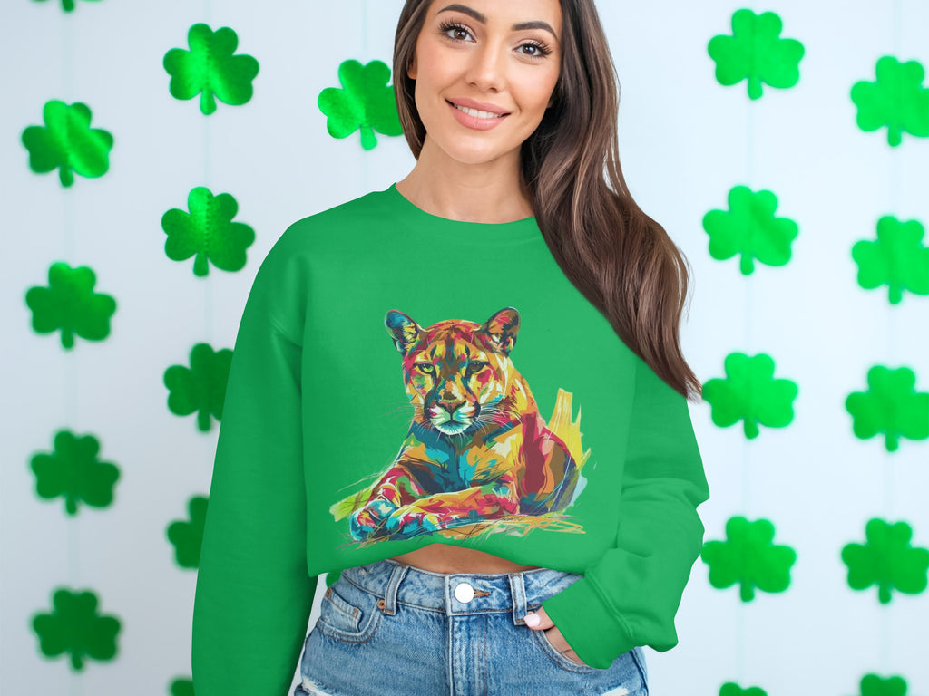 A person with long hair wears a green, unisex Garment Graphics sweatshirt featuring a vibrant colorful cougar design. Green shamrock cutouts on a white wall in the background enhance the unique style.