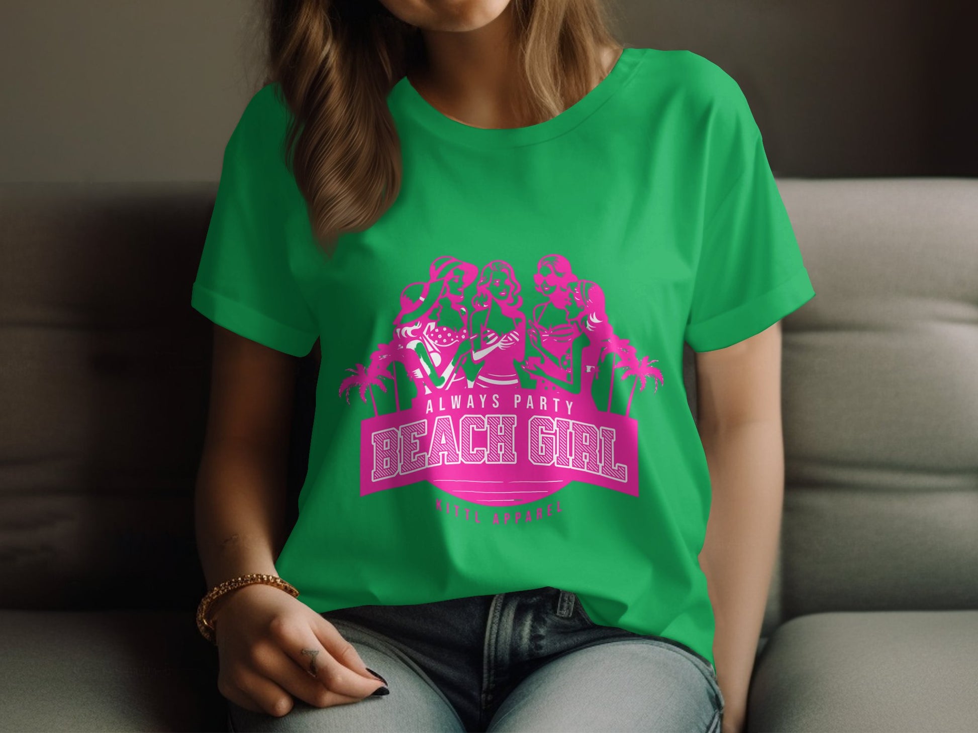 A person lounges on a sofa, wearing a Garment Graphics green T-shirt. The pink graphic shows three styled figures above the text Always Party Beach Girl, with palm tree silhouettes. They gently hold the hem of this Womens Semi-Fitted Tee.
