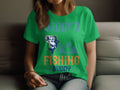 A person relaxes indoors wearing a vibrant green Garment Graphics fishing t-shirt. The shirt says Daddys Fishing Buddy in playful, colorful letters and features a cheerful design of a fish and someone peacefully fishing from a boat.