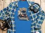 Garment Graphics offers a blue T-shirt with a semi-truck graphic and Keep on Trucking text, ideal for truck enthusiasts. Its styled with a plaid shirt, headphones, camera, and coffee cup on a wooden surface.
