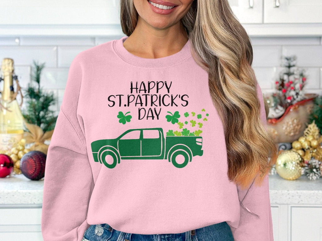 Sporting a pink Garment Graphics festive sweatshirt with a green truck, shamrocks, and Happy St. Patricks Day, one stands by shelves filled with holiday ornaments and a small Christmas tree.