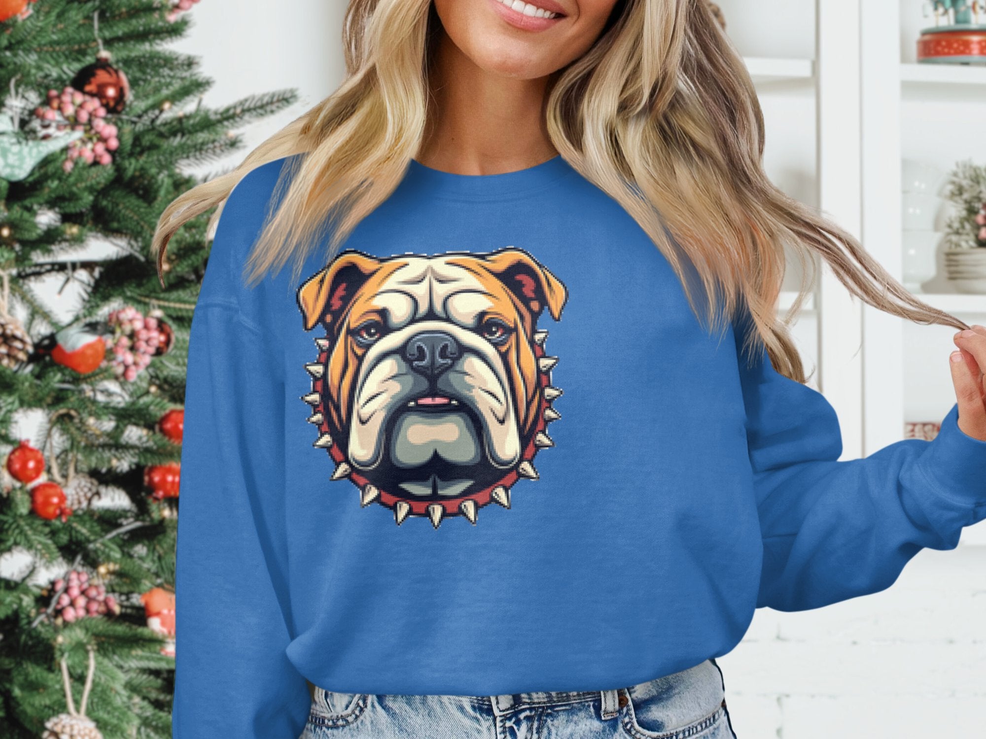 A person in a Garment Graphics blue unisex sweatshirt with a bulldog graphic near a decorated Christmas tree. The stylized bulldog head features a spiked collar, adding flair to the festive scene, though the persons face is partially out of frame.