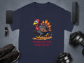 A navy blue Garment Graphics T-shirt with a classic fit features a cartoon turkey running with Turkey on the Run text. It is displayed on a gray surface surrounded by a smartphone, smartwatch, Bluetooth speaker, black shoes, and adjustable dumbbells.