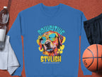 The Garment Graphics blue sweatshirt showcases a vibrant dog graphic, complete with sunglasses and the playful phrases Pawsitive Stylish and Chillin Like a Canine Villain. Ideal for dog enthusiasts, its depicted amidst a sporty scene with a water bottle, towel, shorts, and basketball on red.
