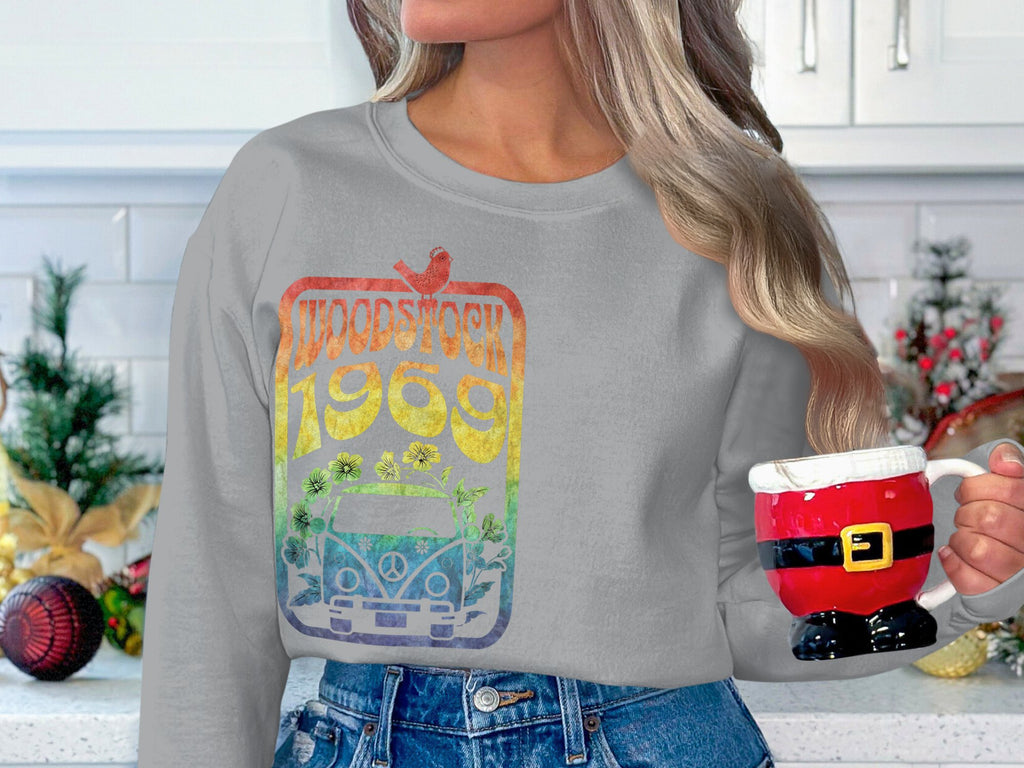 In a kitchen with holiday decor and a red ornament, someone exudes retro style in blue jeans and a Garment Graphics Woodstock 1969 gray sweatshirt with a vibrant design, while holding a Santa-themed mug.