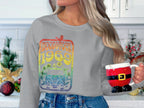 In a kitchen with holiday decor and a red ornament, someone exudes retro style in blue jeans and a Garment Graphics Woodstock 1969 gray sweatshirt with a vibrant design, while holding a Santa-themed mug.