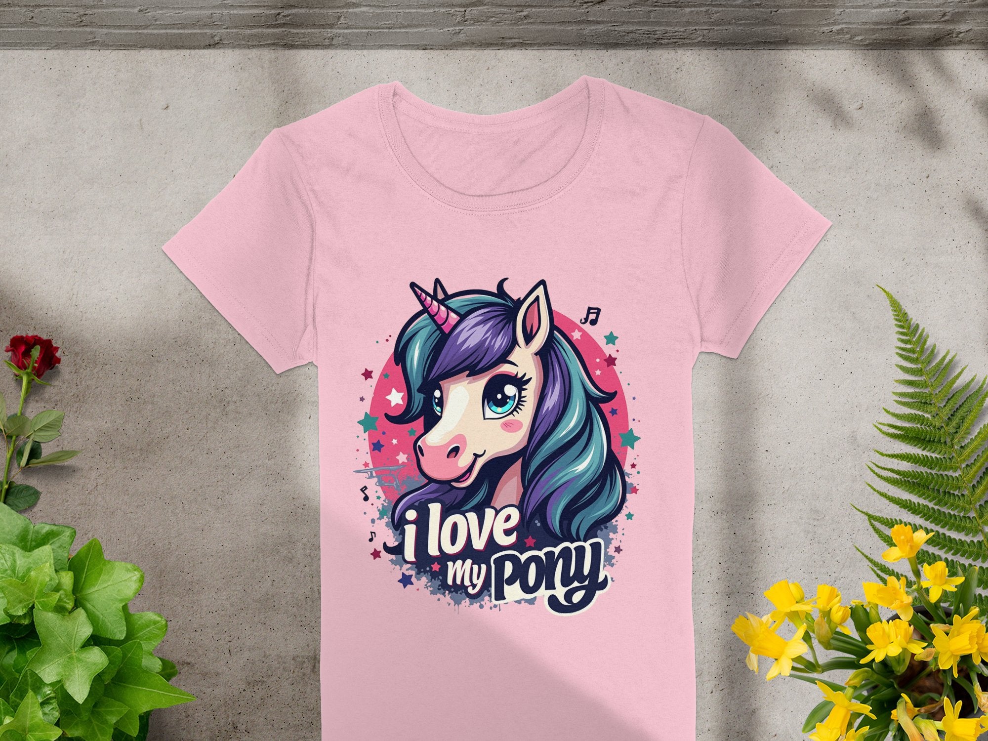 This cute pink t-shirt by Garment Graphics is perfect for unicorn lovers, featuring a unicorn graphic with a purple mane, stars, and music notes. With I Love My Pony text, its displayed on concrete with vibrant green and yellow plants, capturing the whimsical spirit beautifully.